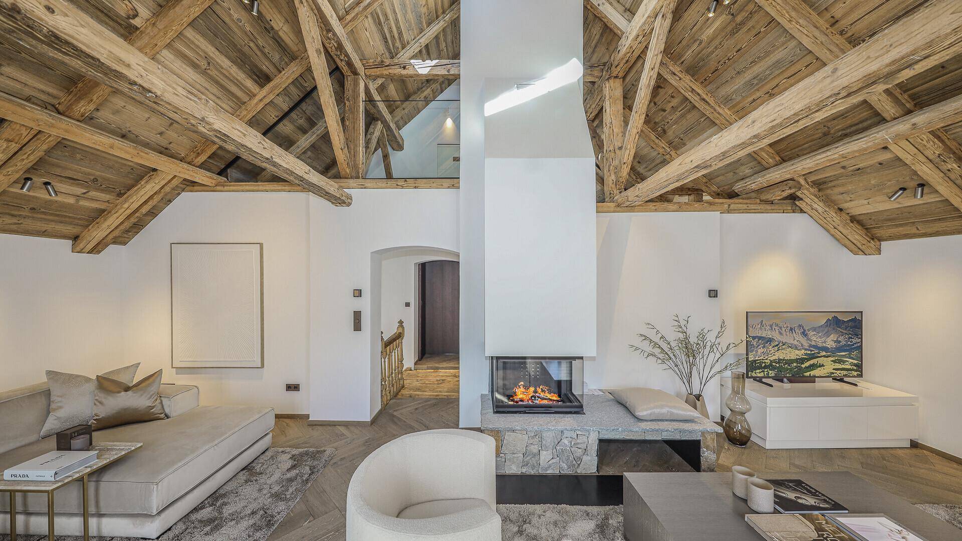 Offener Wohnbereich mit beeindruckendem Kamin, hohen Decken und sichtbaren Holzbalken.