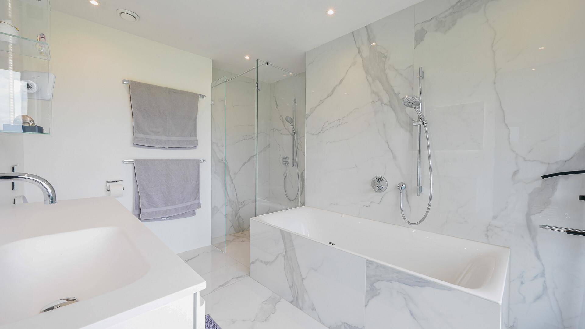 Modernes Badezimmer mit Marmorfliesen, Badewanne und begehbarer Dusche.