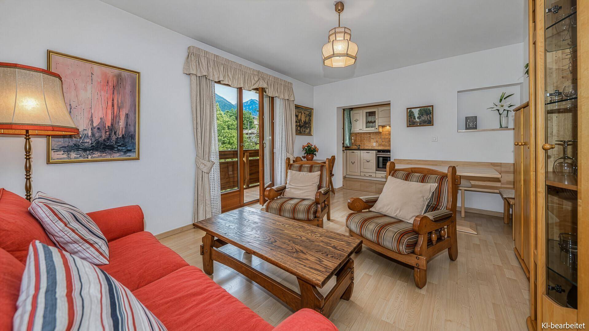 Gemütliches Wohnzimmer mit rotem Sofa, Holztisch und Balkonzugang, offen zum Essbereich und zur Küche.