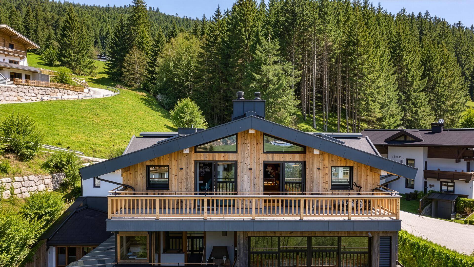 Vorderansicht eines modernen Chalets mit Holzfassade, großen Fenstern und Balkon.