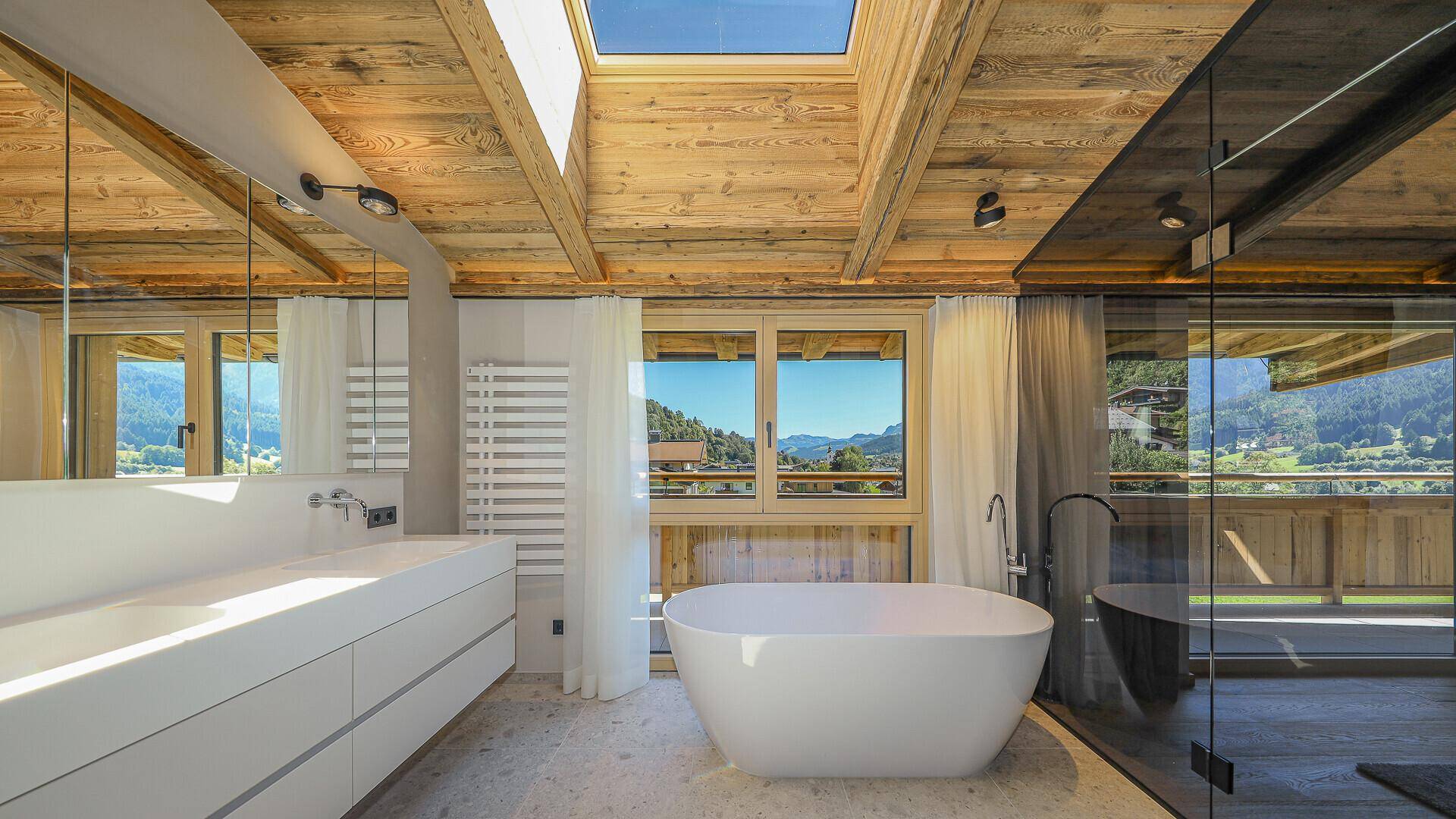 Helles Badezimmer mit freistehender Badewanne, Doppelwaschbecken und Bergblick durch große Fenster.