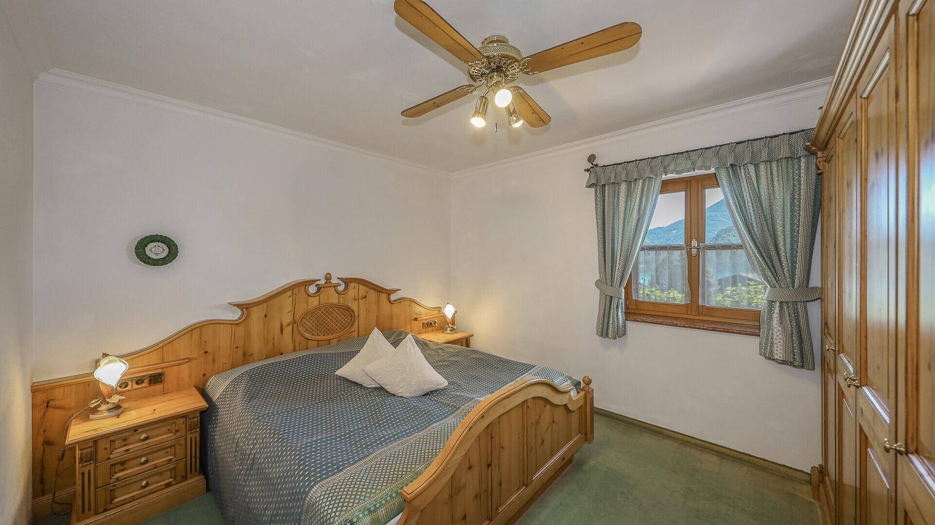 Gemütliches Schlafzimmer im traditionellen Stil mit Holzmöbeln, Teppichboden und Deckenventilator.