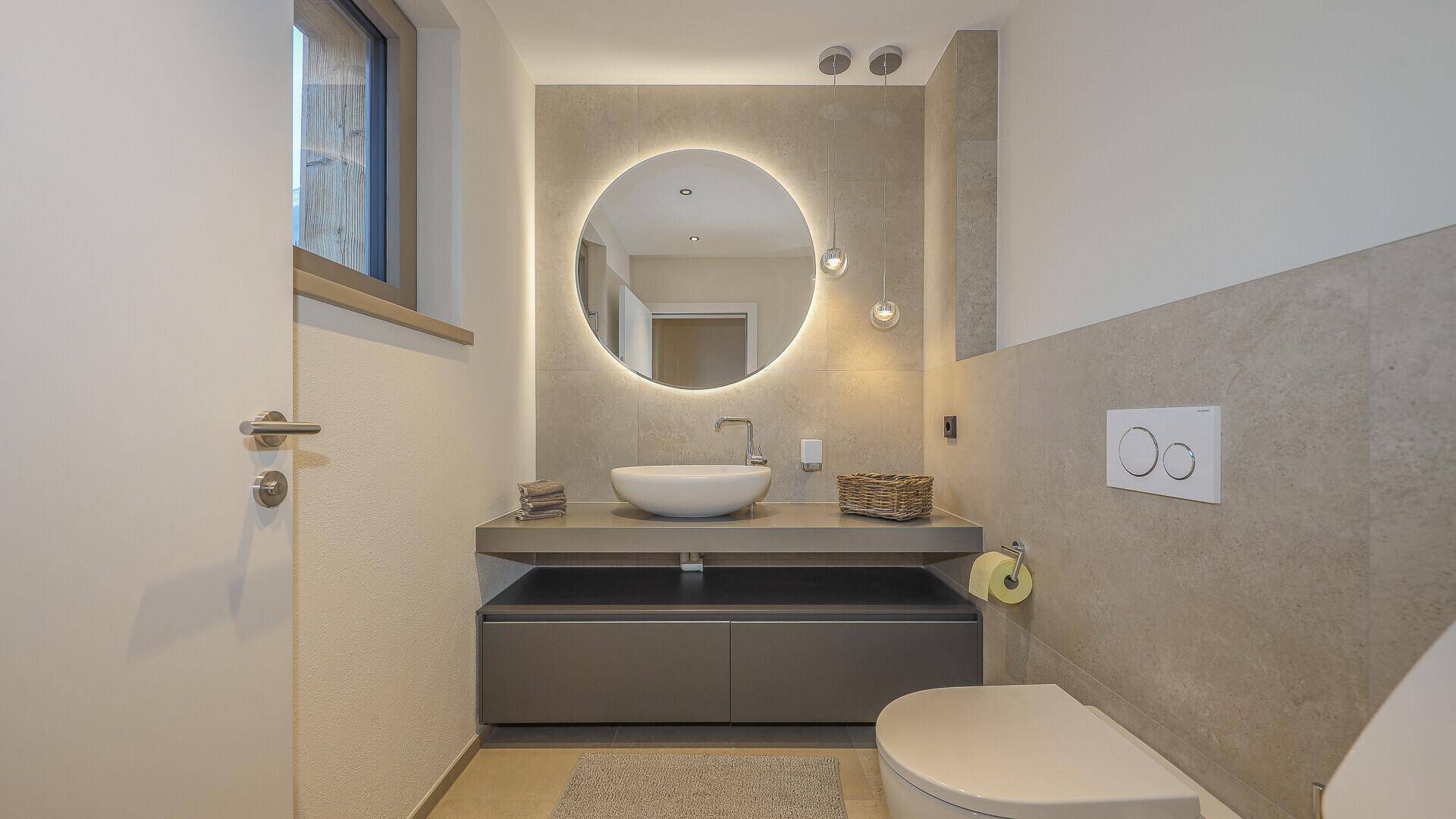Modernes Gäste-WC mit rundem Spiegel, Aufsatzwaschbecken und Wand-WC.