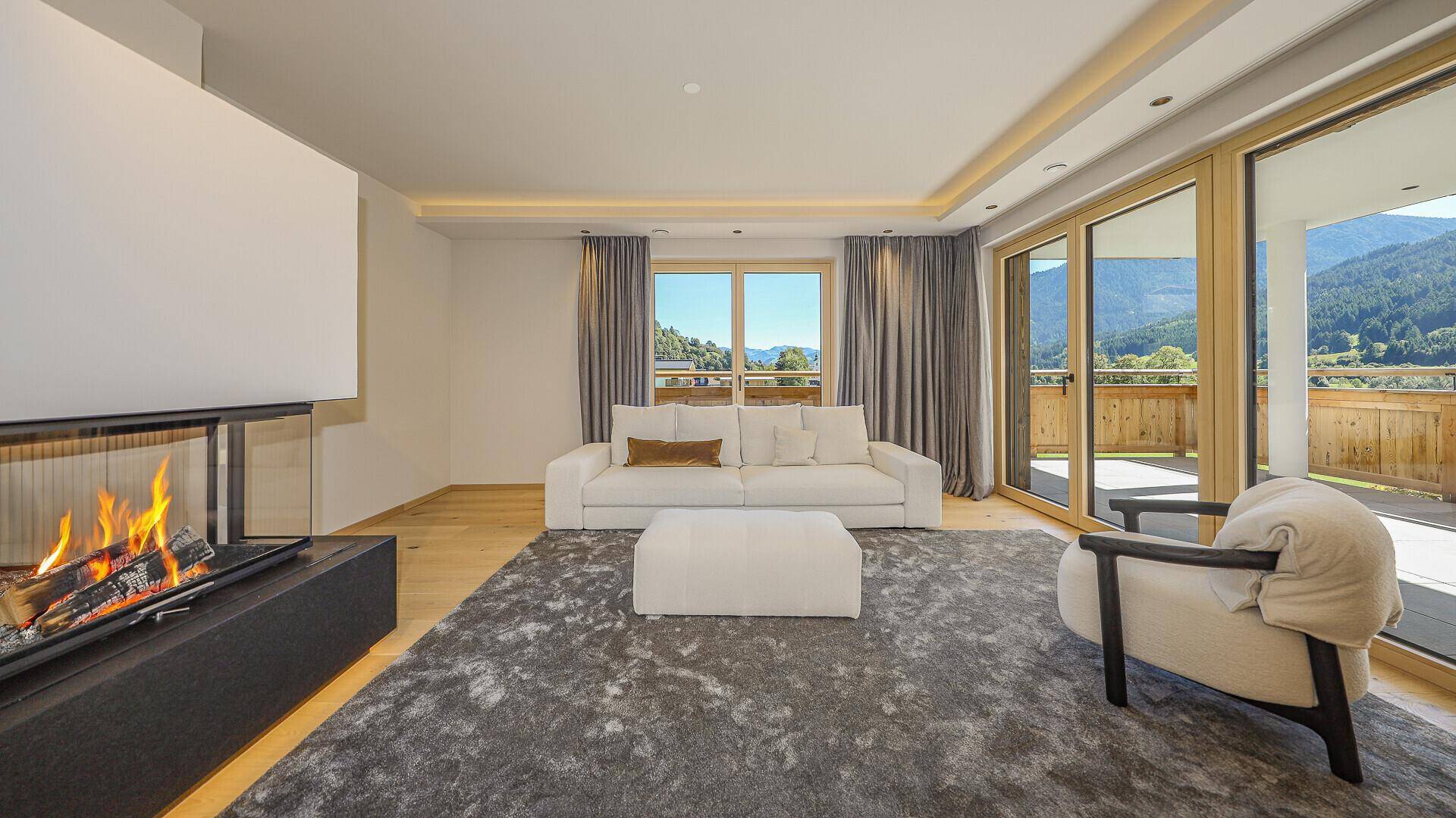 Gemütliches Wohnzimmer mit Kamin, weichen Möbeln und großen Fenstern mit Alpenblick.