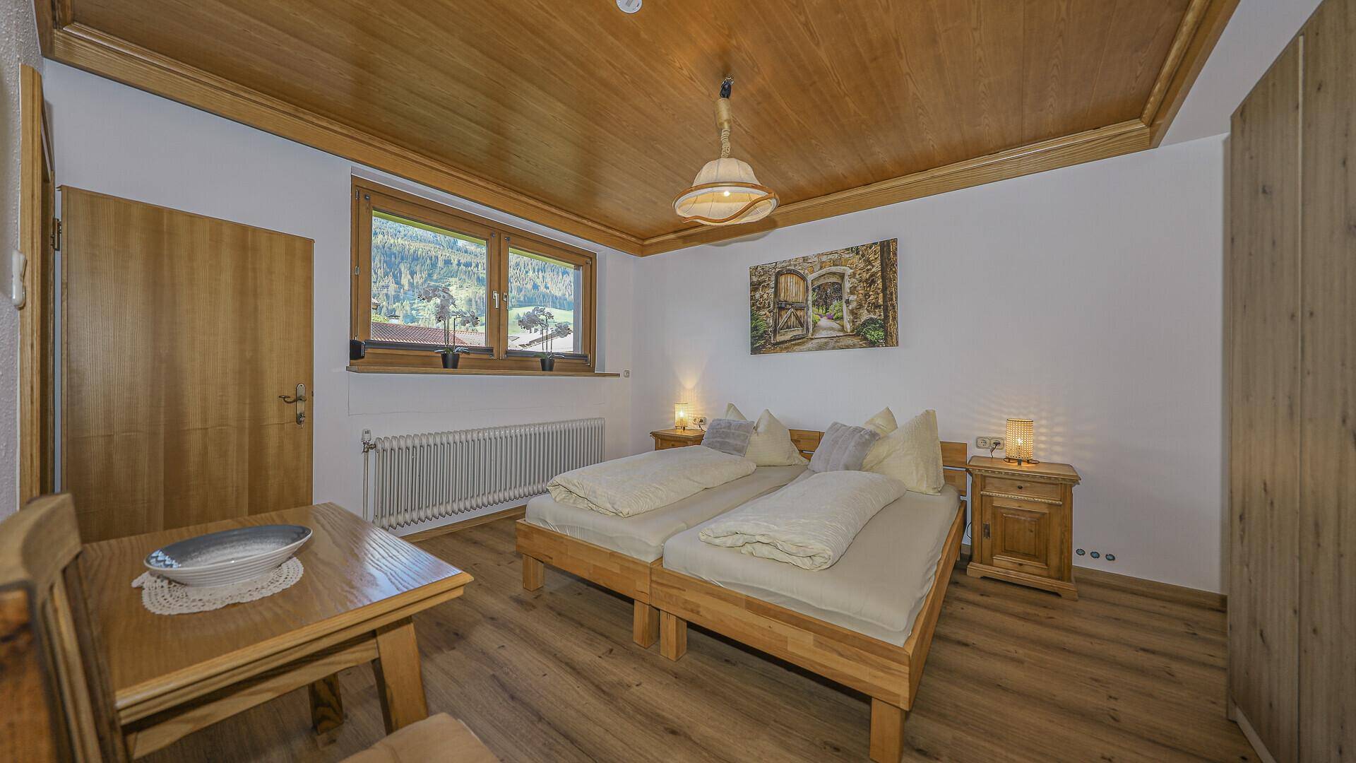 Gemütliches Schlafzimmer mit Holzdecke, Doppelbett und Blick auf die grüne Berglandschaft.
