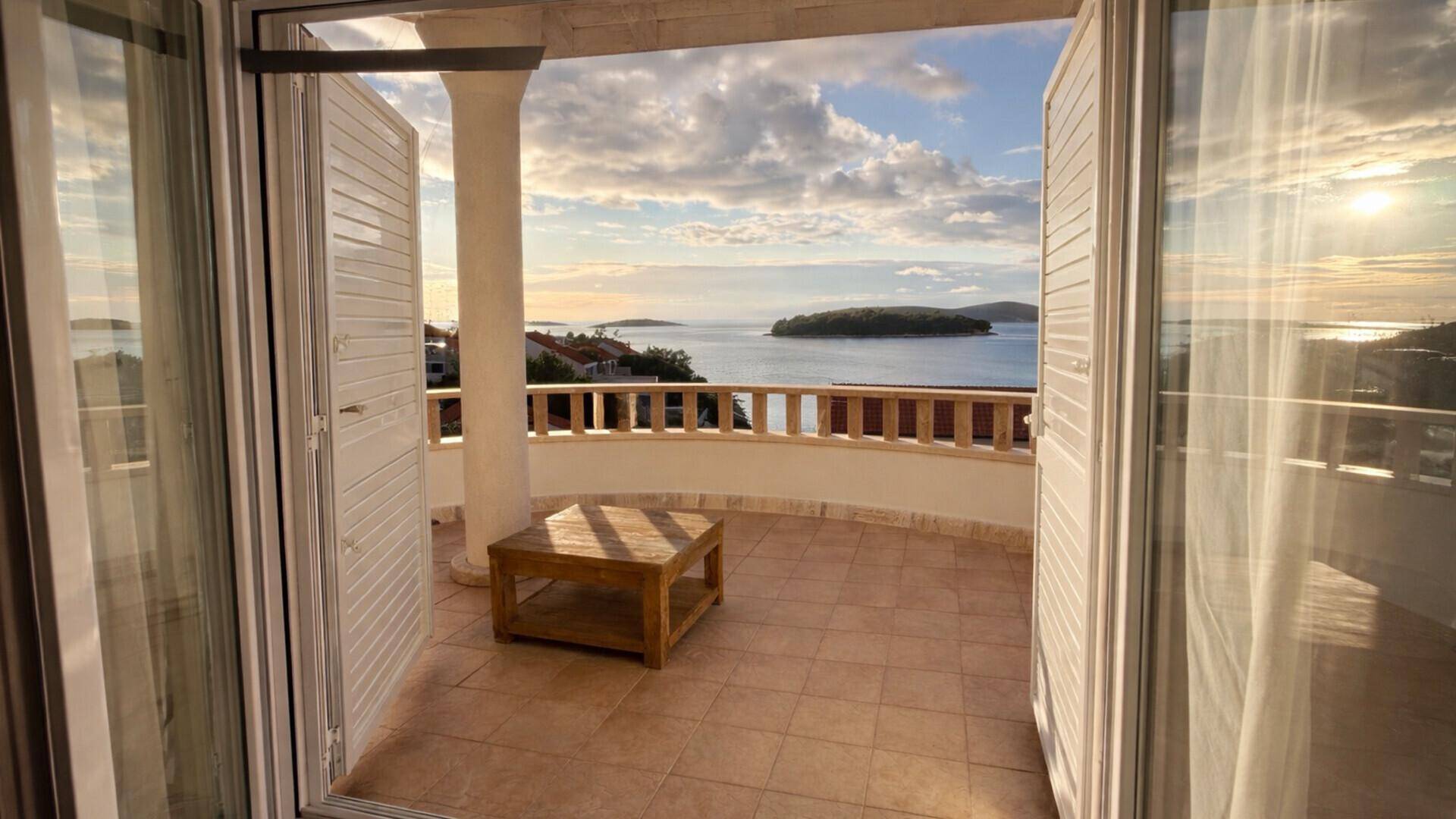 Blick vom Innenraum auf einen möblierten Balkon mit Tisch und weitem Meerblick.