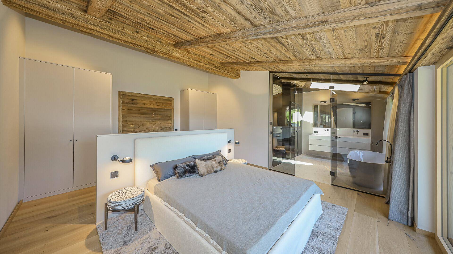 Modernes Schlafzimmer mit Holzbalkendecke, Einbauschränken und offenem Badbereich mit Badewanne.