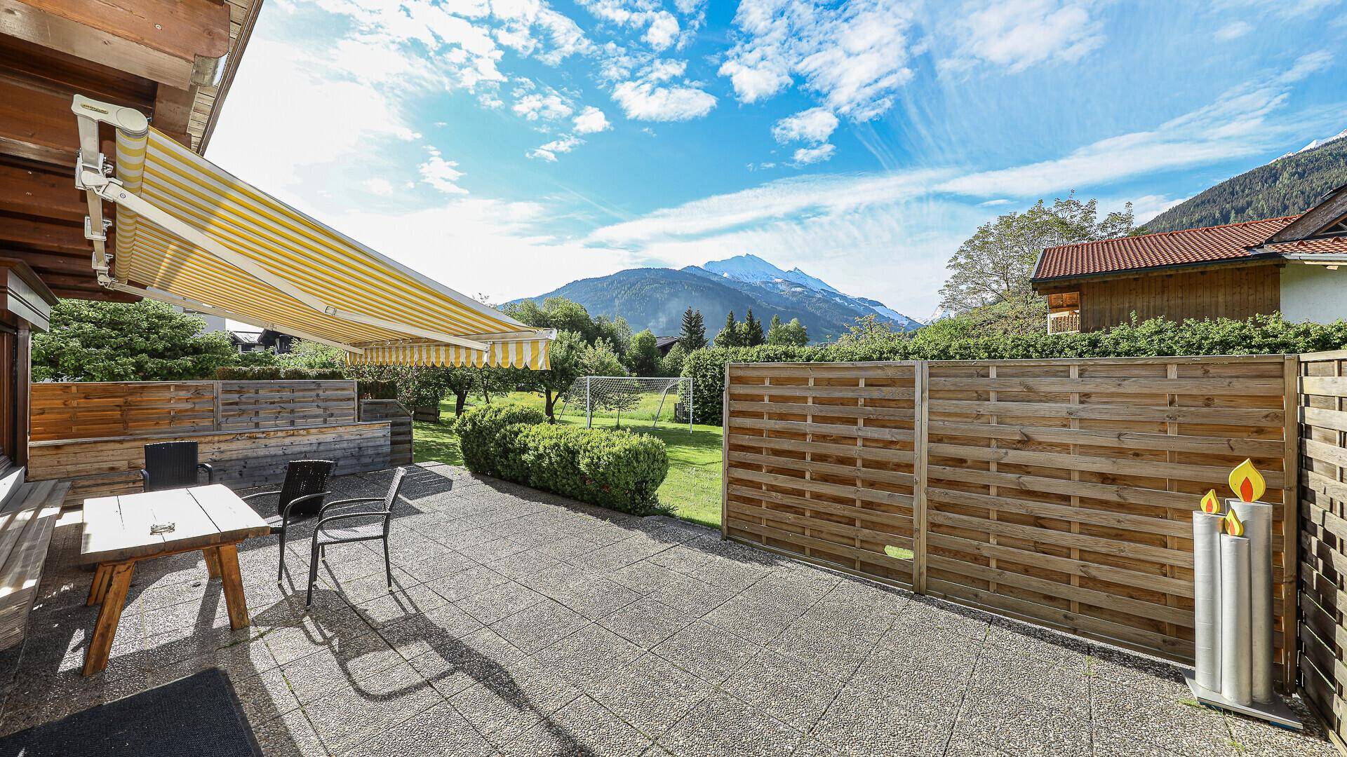 Sonnenterrasse mit Gartenmöbeln, Markise und herrlichem Blick auf die umliegenden Berge.