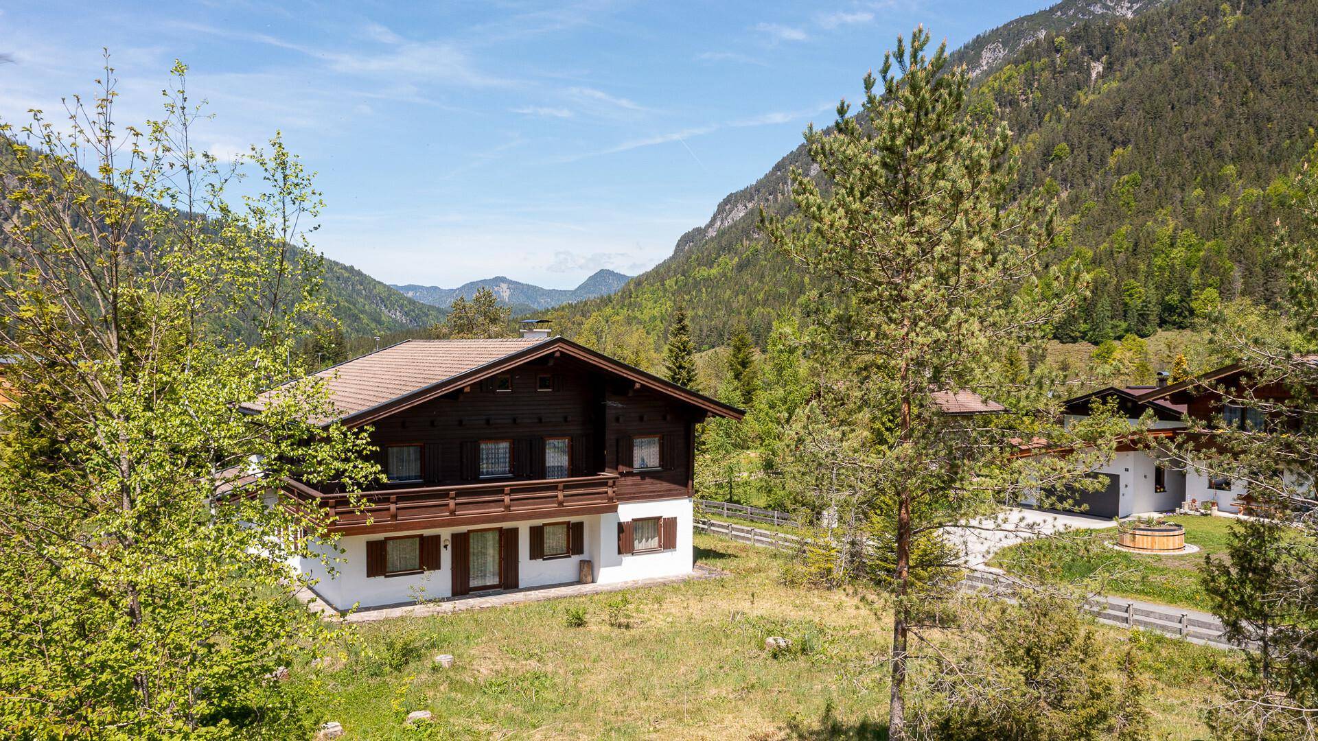 Luftaufnahme eines traditionellen Chalets mit Satteldach, umgeben von grünen Bäumen und Bergen.