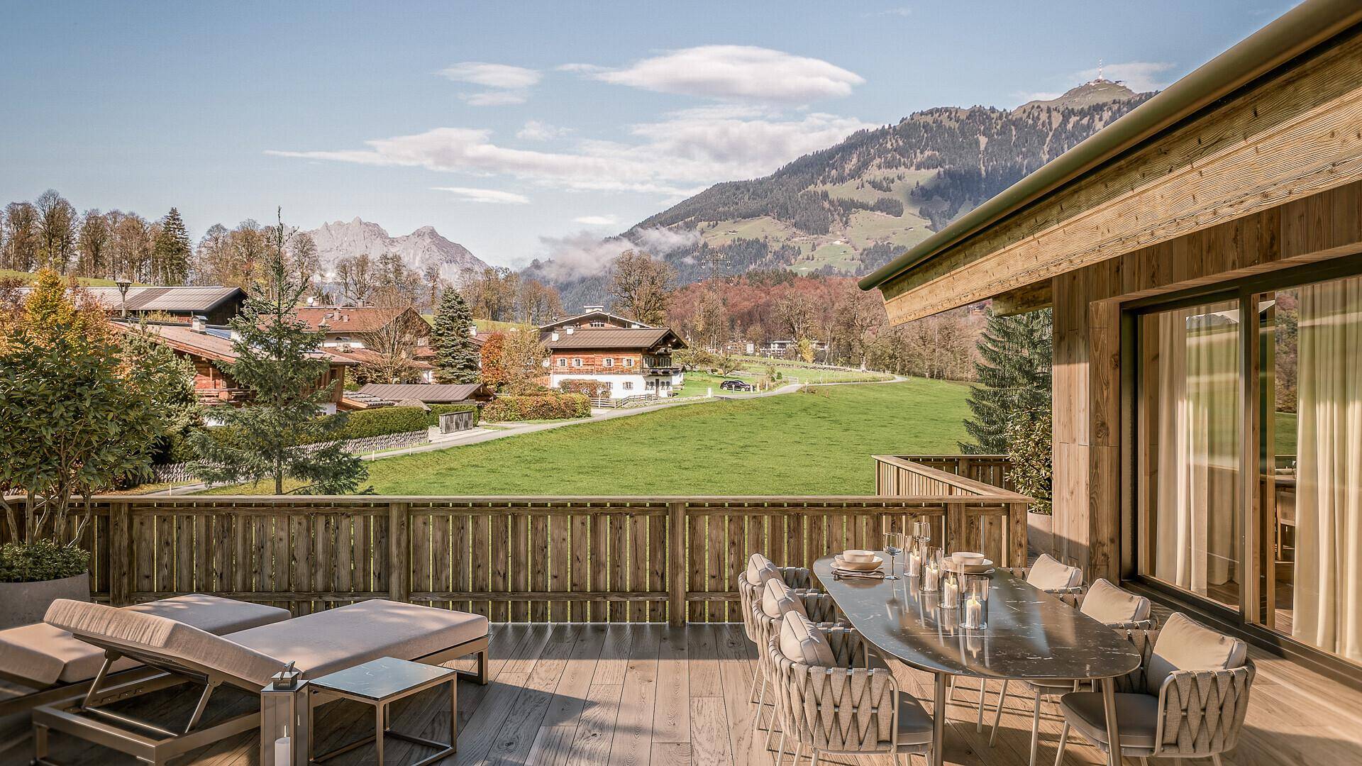 Geräumige Holzterrasse mit Essbereich und Liegestühlen, umgeben von grüner Landschaft und Bergblick.
