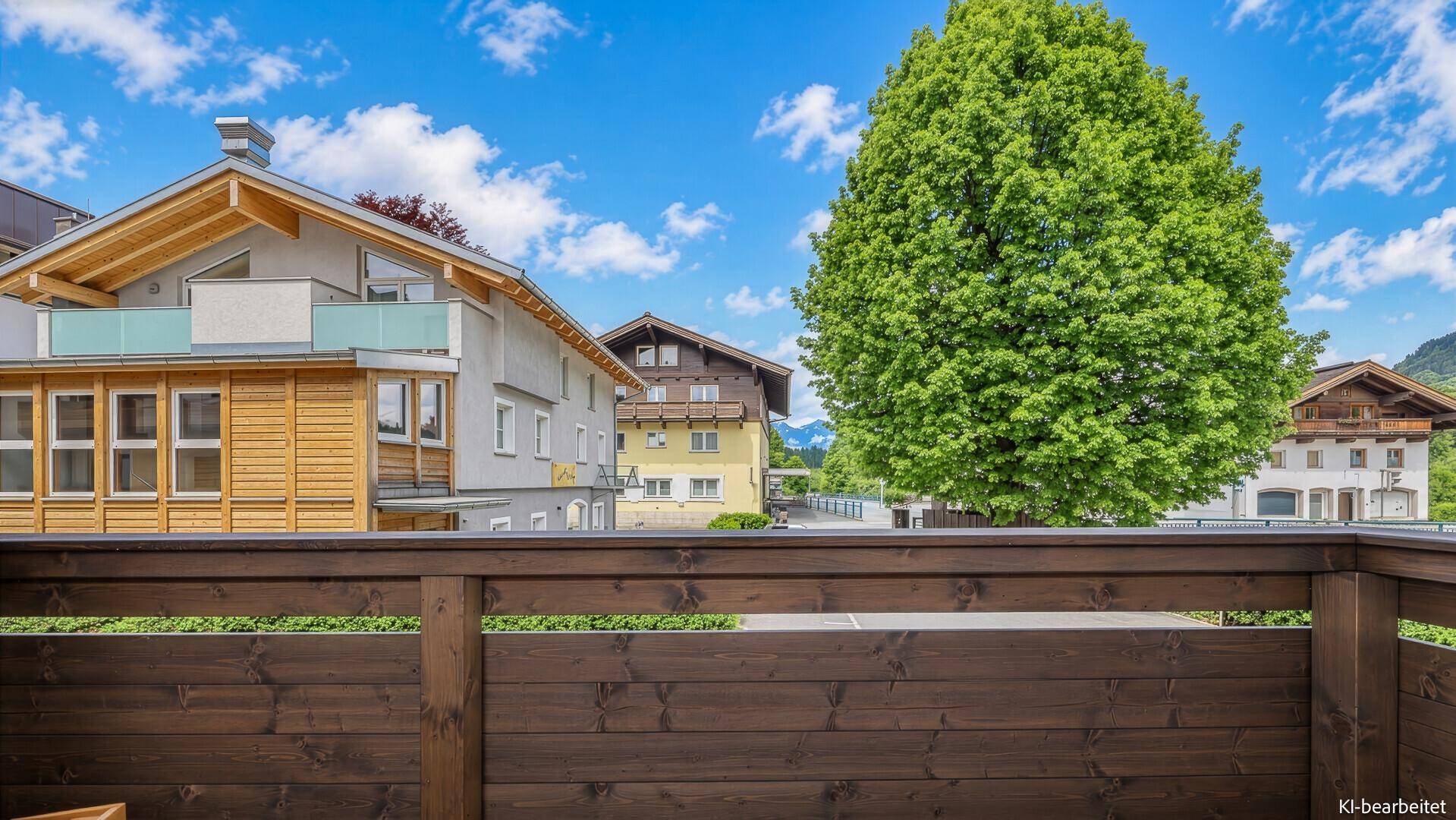 Balkon mit Holzgeländer und Blick auf umliegende Gebäude und Bäume.