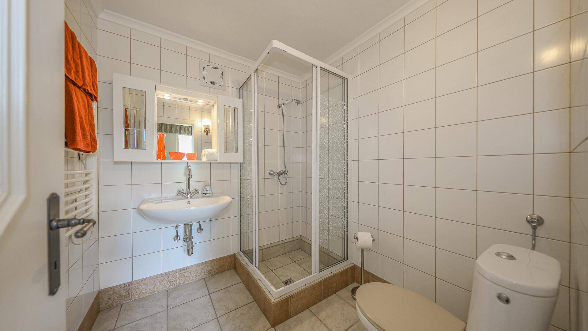 Badezimmer mit Duschkabine, Waschbecken, Toilette und weißen Wandfliesen.