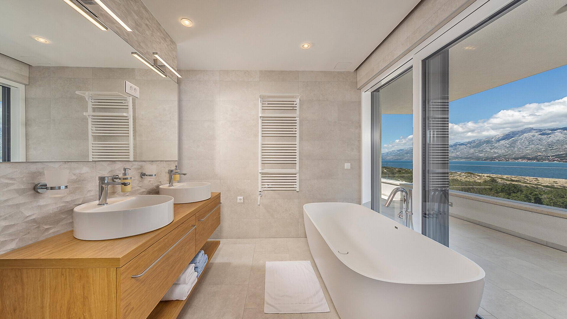 Modernes Badezimmer mit freistehender Badewanne, Doppelwaschbecken und großen Fenstern mit Meerblick.