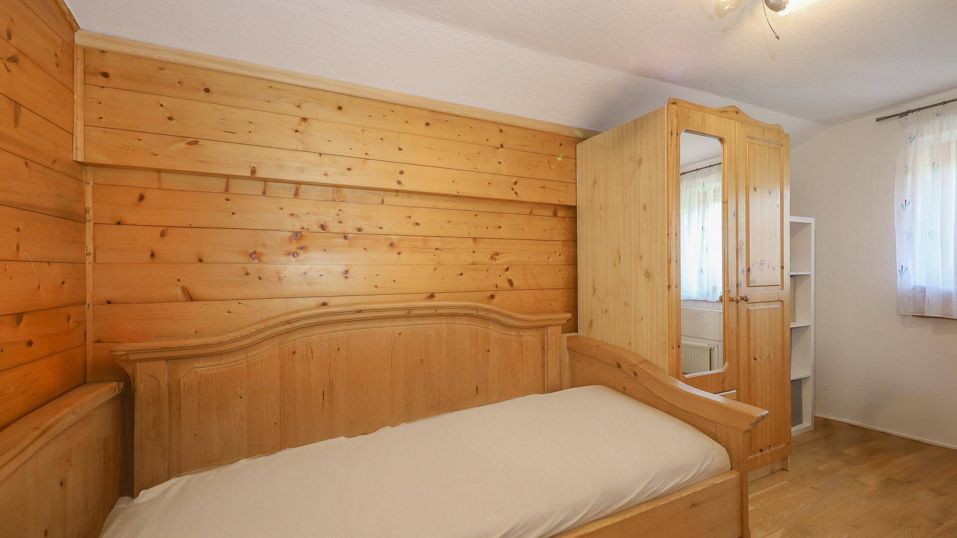 Schlafzimmer mit Holzwänden, Einzelbett und Kleiderschrank, einfach und funktional.