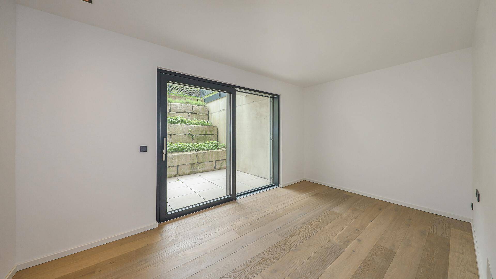 Helles Zimmer mit Holzboden und Zugang zu einem terrassierten Außenbereich.
