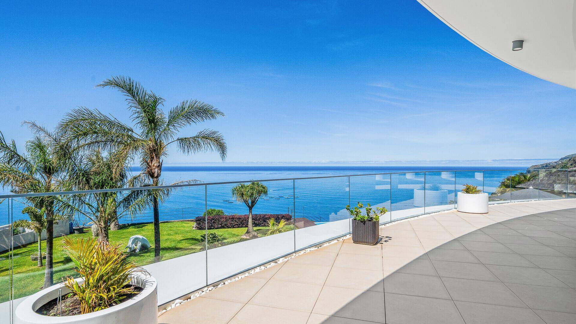 Weitläufige Terrasse mit Panoramablick auf das Meer, Palmen und einem eleganten Glasgeländer.
