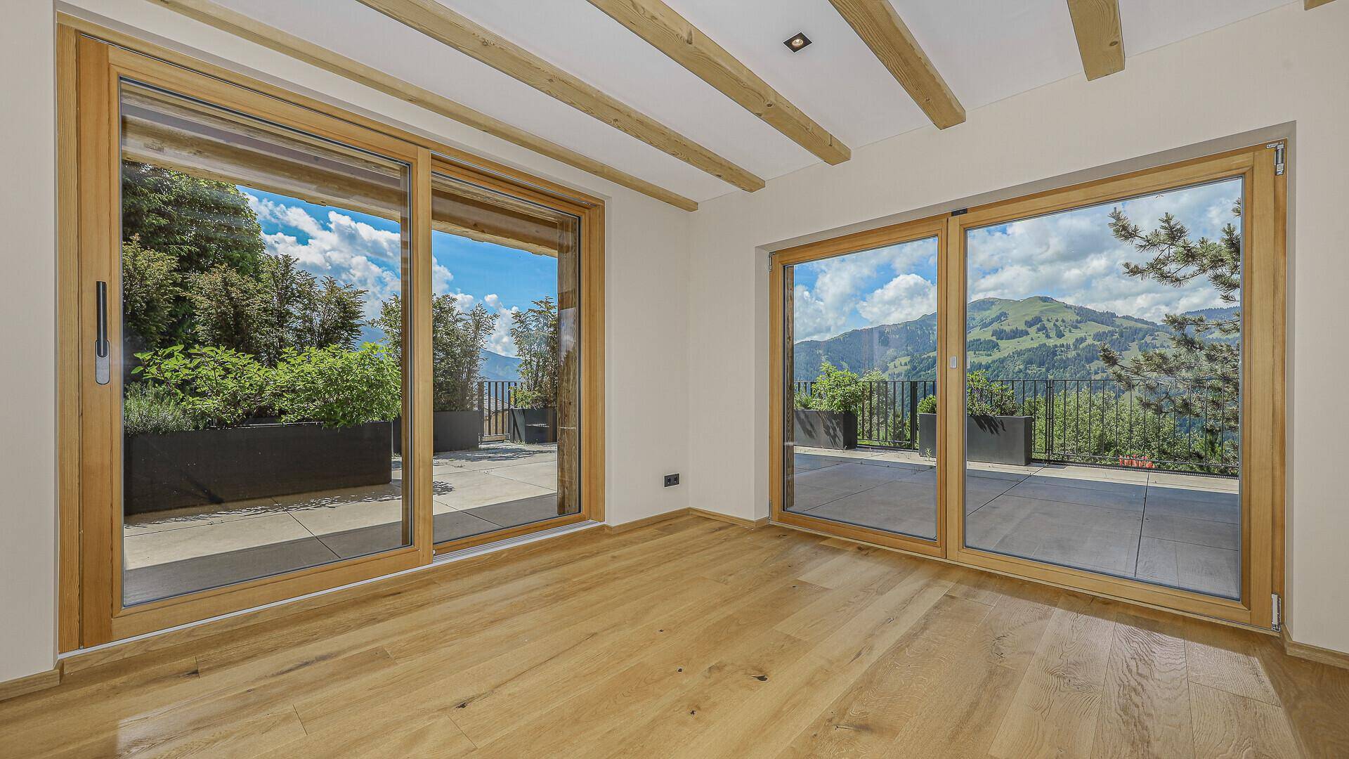 Heller Wohnraum mit Holzbalkendecke, Eichenparkett und Zugang zur Terrasse mit Bergblick.