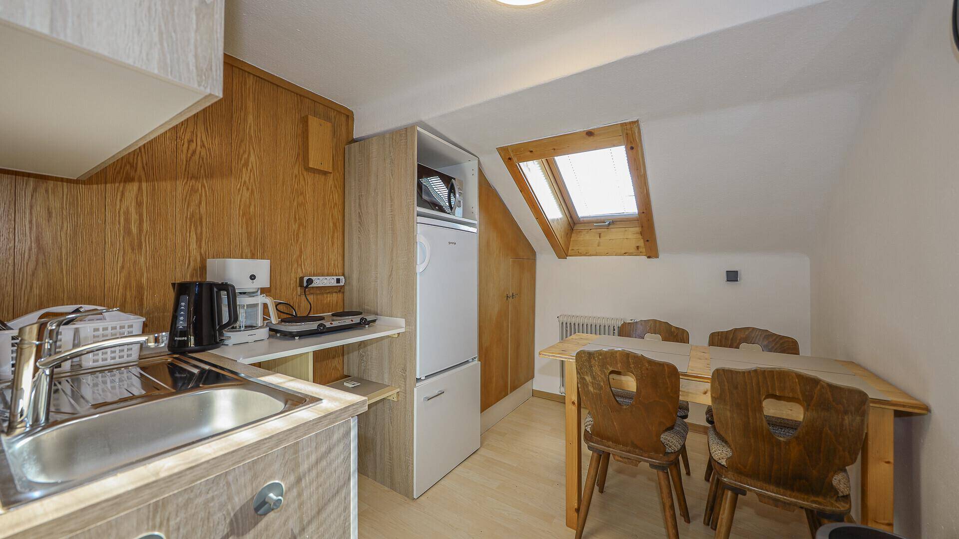 Kleine Dachgeschoss-Küchenzeile mit Essbereich, Kühlschrank und Dachfenster.