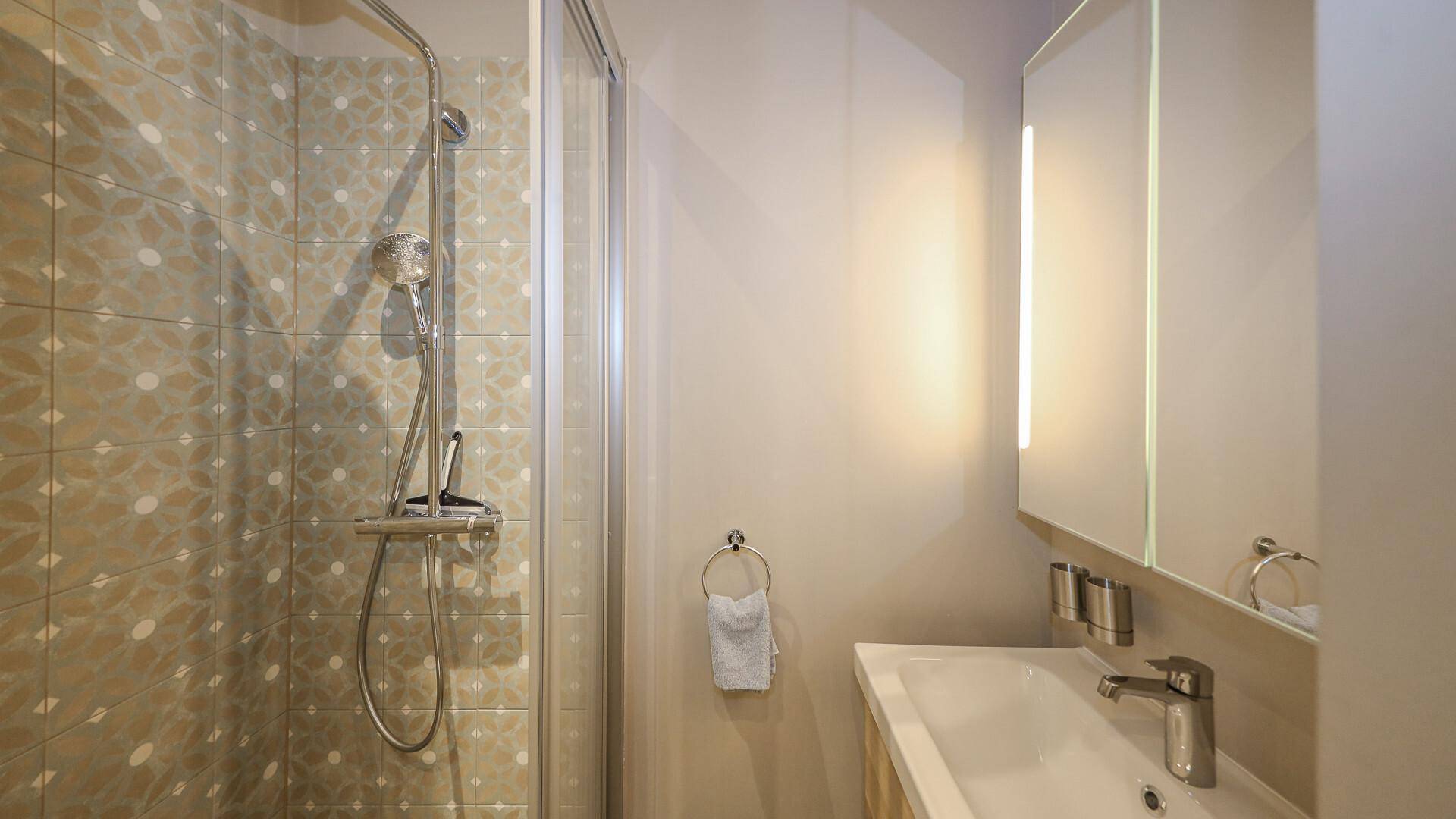 Badezimmer mit Duschkabine, Waschbecken und Spiegelschrank, hell und funktional.
