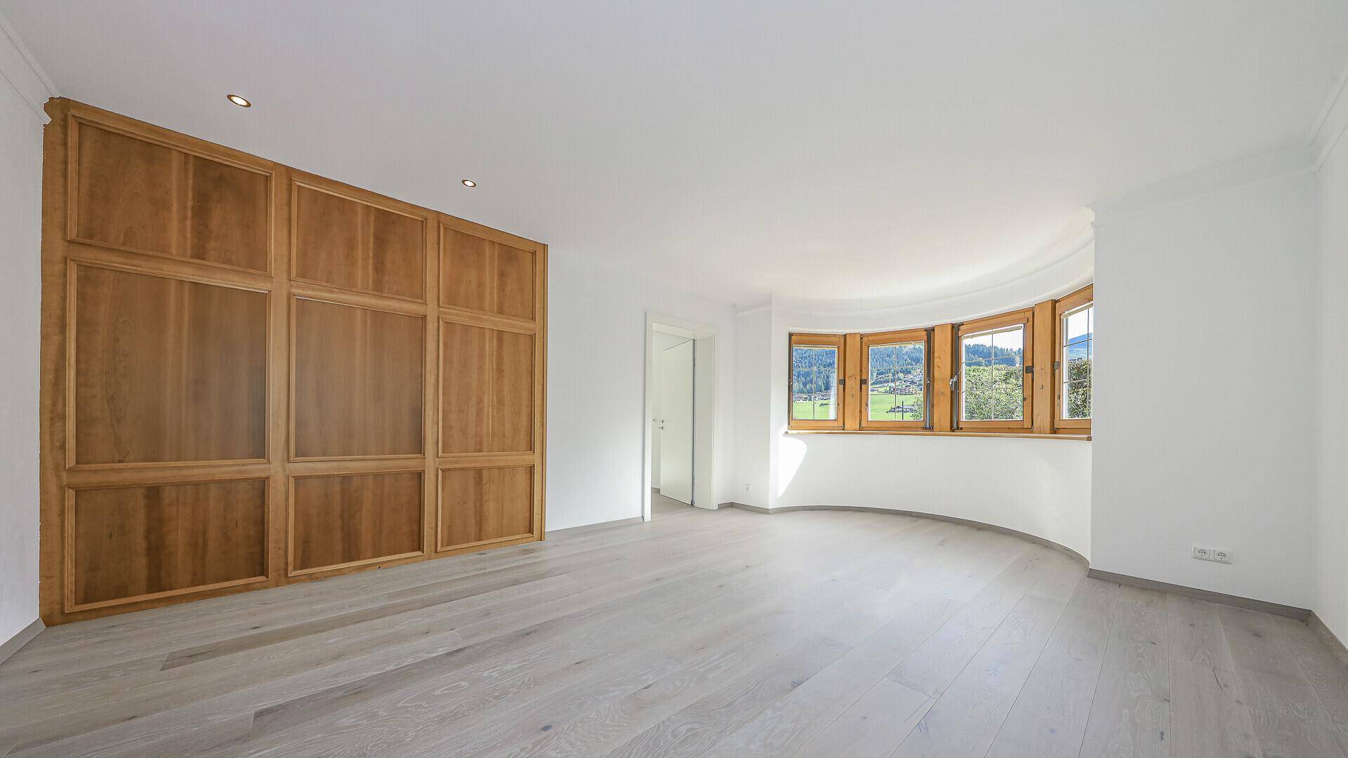 Geräumiges, helles Wohnzimmer mit Holzboden und großen Fenstern, die viel Tageslicht hereinlassen.