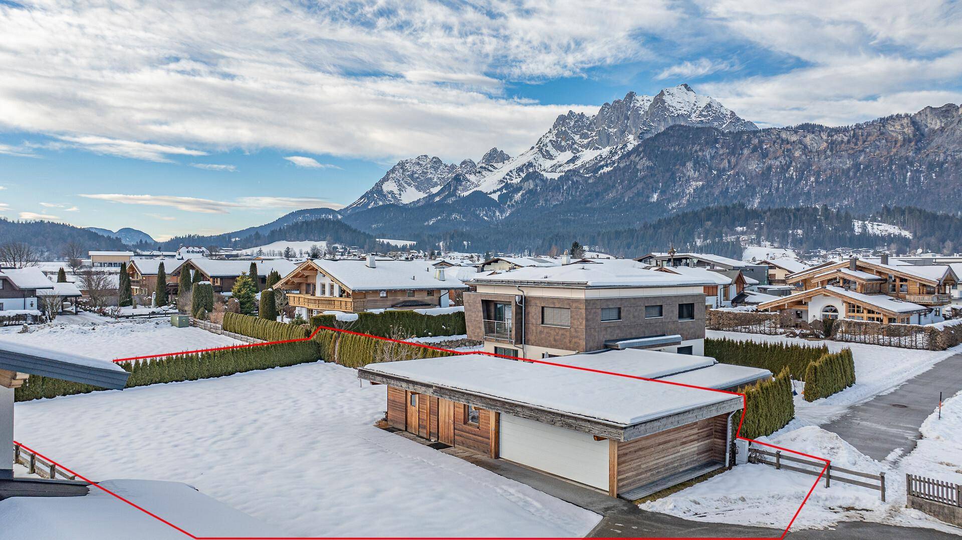 Luftaufnahme eines Grundstücks mit Garage und umliegenden Häusern in verschneiter Berglandschaft.