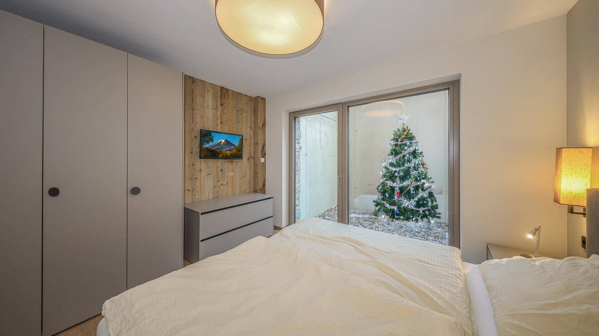 Gemütliches Schlafzimmer mit Holzwand, Einbauschränken und Blick auf einen festlich geschmückten Baum.