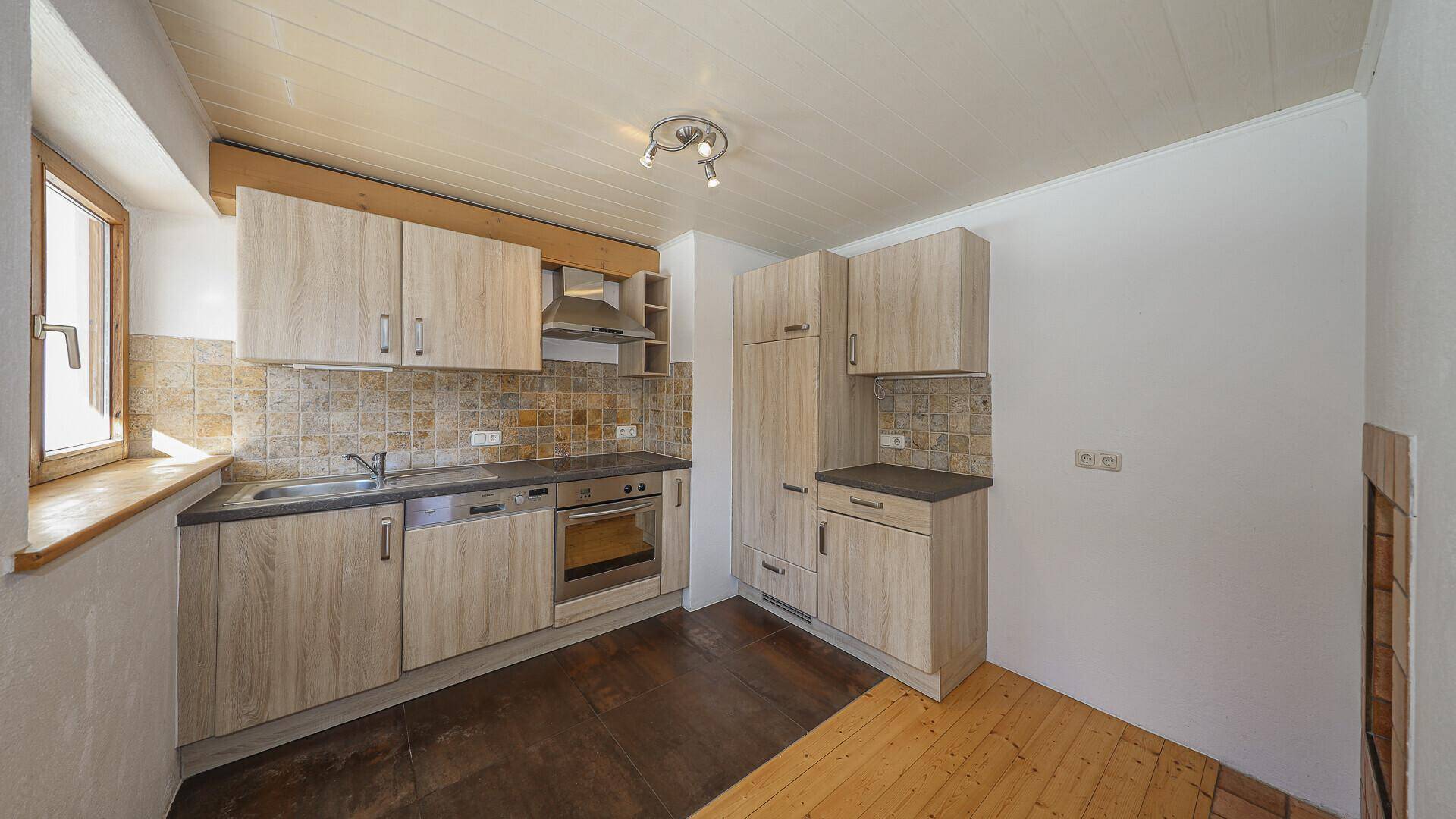 Funktionale Küche mit Holzschränken, Fliesenrückwand und Fensterblick ins Grüne.