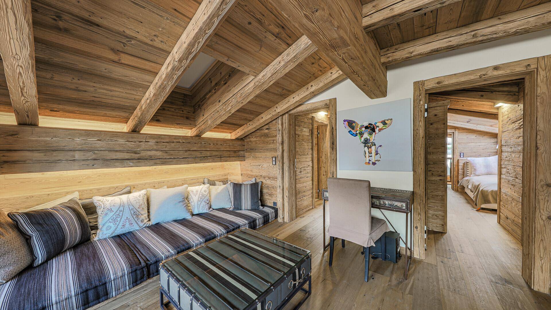 Dachgeschoss-Wohnbereich mit sichtbaren Holzbalken, gemütlicher Sitzecke und Schreibtisch.