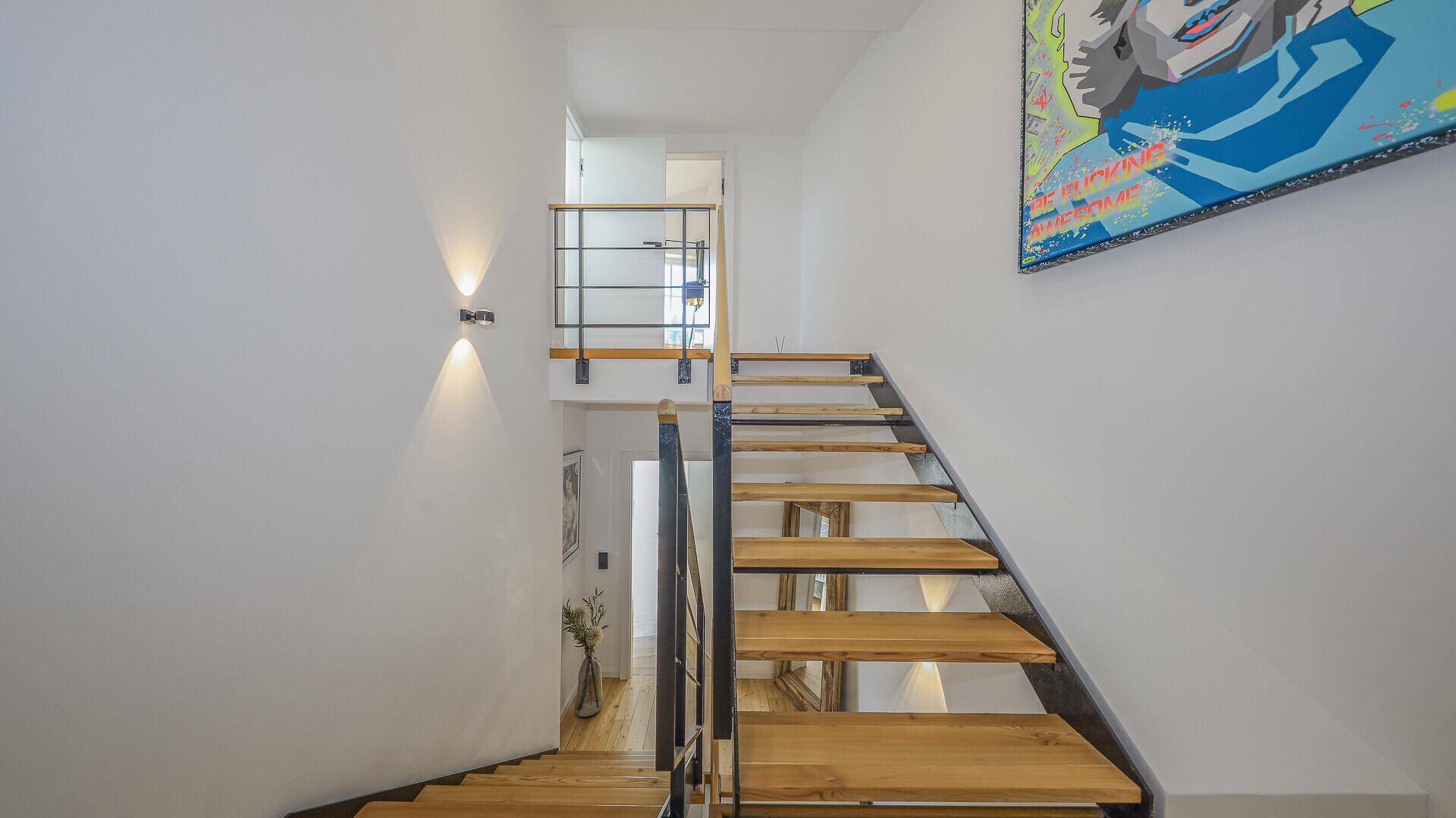 Moderne Holztreppe mit schlankem Metallgeländer, die zu den oberen Etagen des Hauses führt.