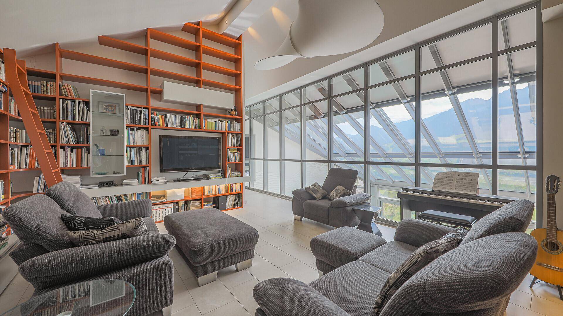Geräumiges Wohnzimmer mit Bücherregalen, Fernseher und großen Fenstern mit Bergblick.