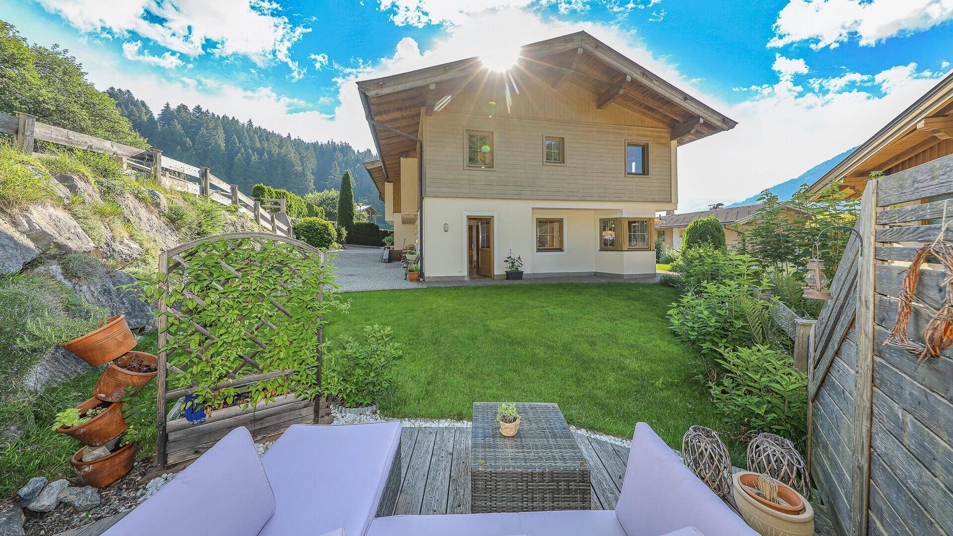 Gepflegter Gartenbereich mit großer Rasenfläche und gemütlicher Holzterrasse vor dem Haus.