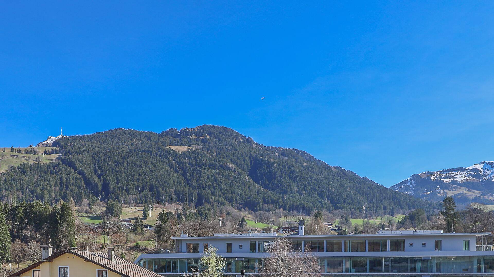 Weitläufiger Blick auf bewaldete Berge und ein modernes Gebäude mit großen Glasfronten im Tal.