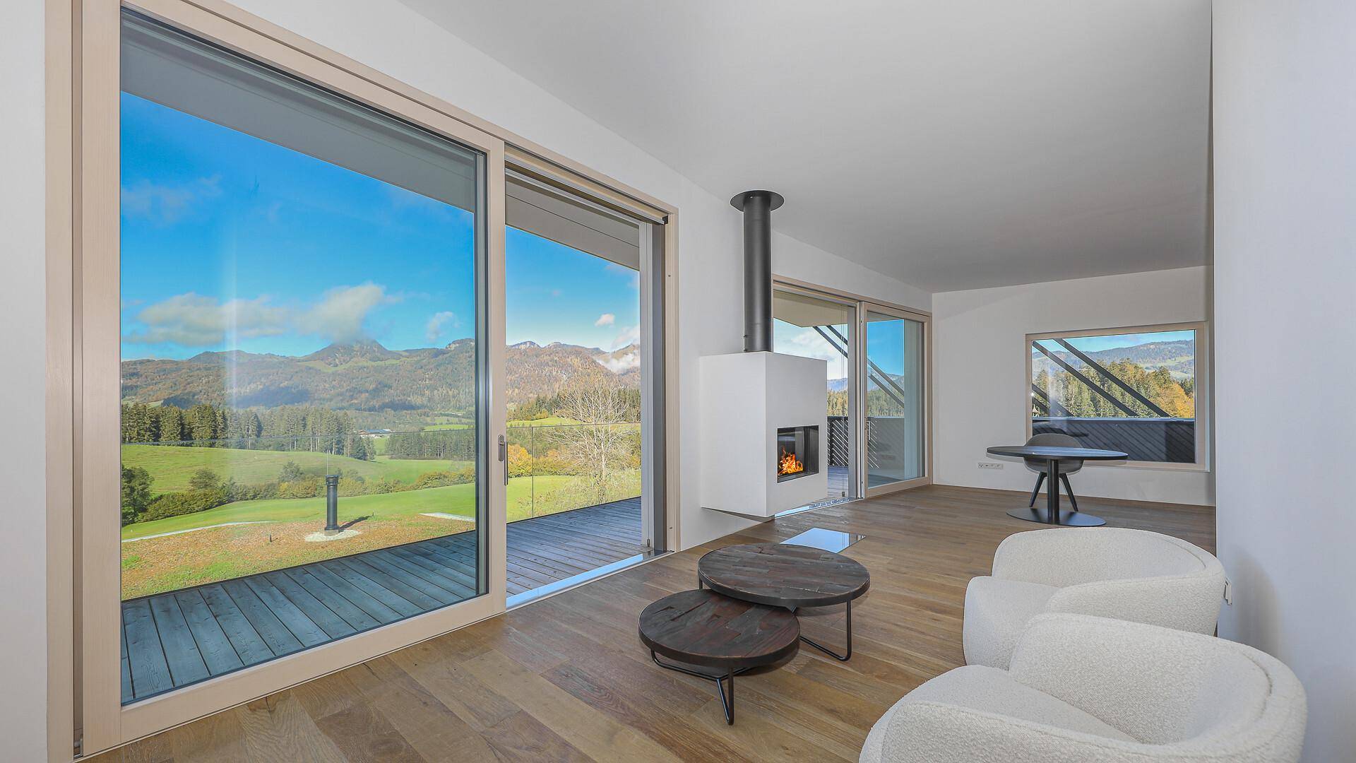 Lichtdurchflutetes Wohnzimmer mit Kamin, Holzboden und weitem Blick auf die Berglandschaft.