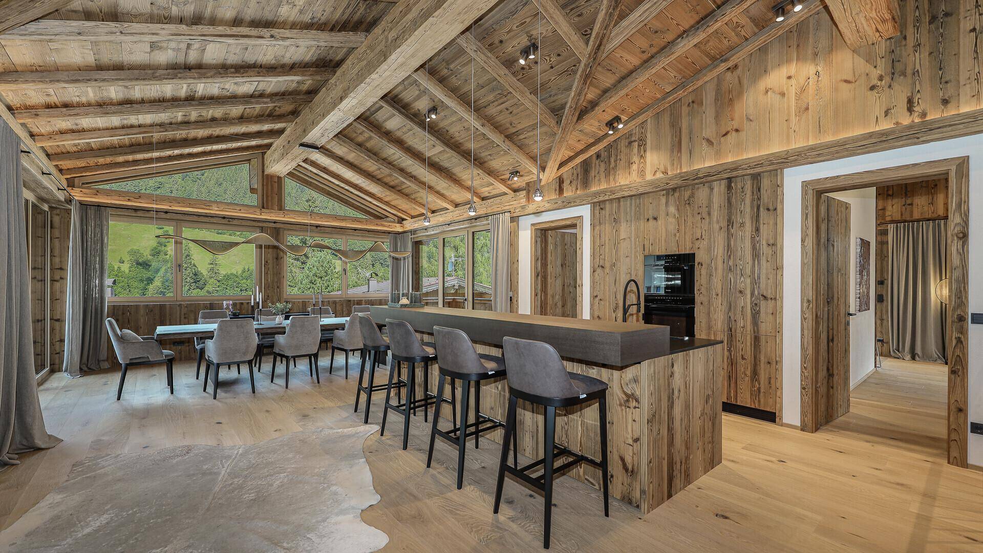 Eleganter Essbereich mit Holztisch, modernen Stühlen und großen Fenstern mit Bergblick.