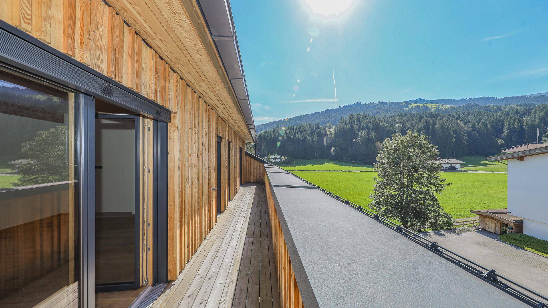 Seitenansicht eines modernen Gebäudes mit Holzfassade und Flachdach vor grüner Bergkulisse.