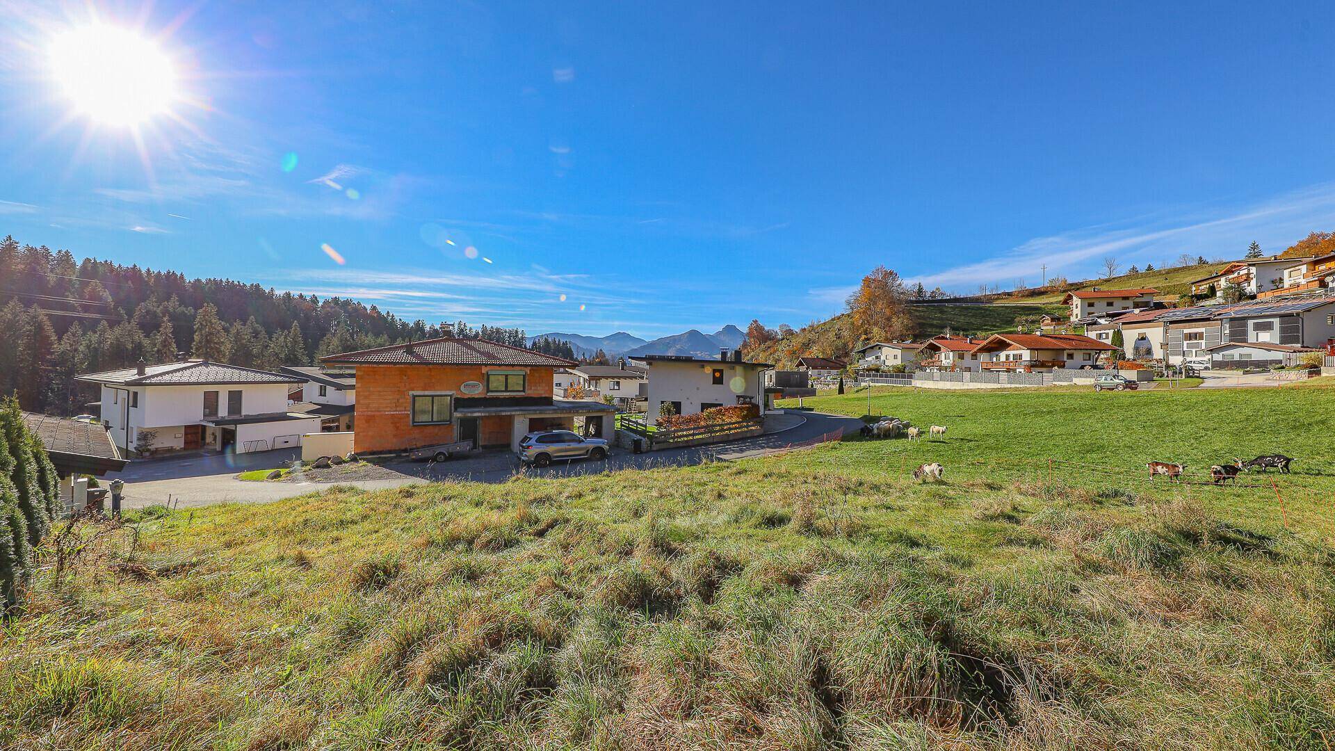 Sonnige Wiesen mit Häusern und Bergen im Hintergrund, ideal für Naturliebhaber.