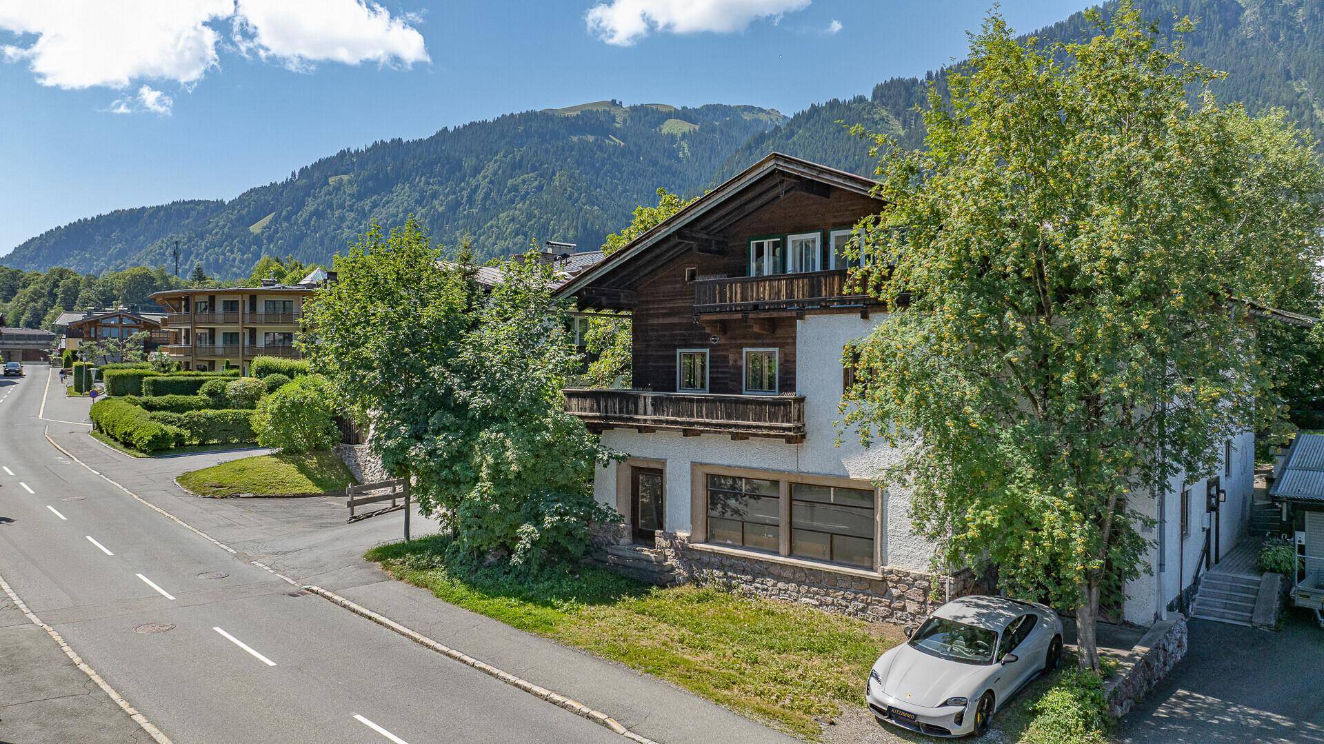 Traditionelles Haus mit Holzbalkonen und weißer Fassade, umgeben von üppigem Grün und Bergen.