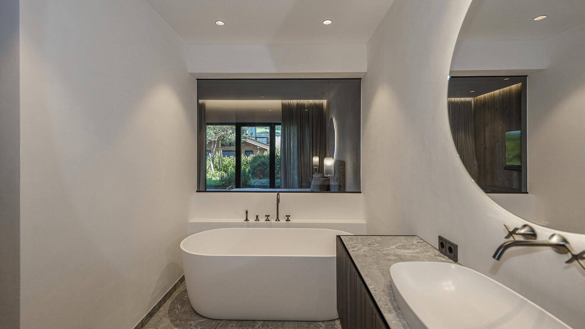 Helles Badezimmer mit freistehender Badewanne, modernem Waschtisch und großem Fenster.