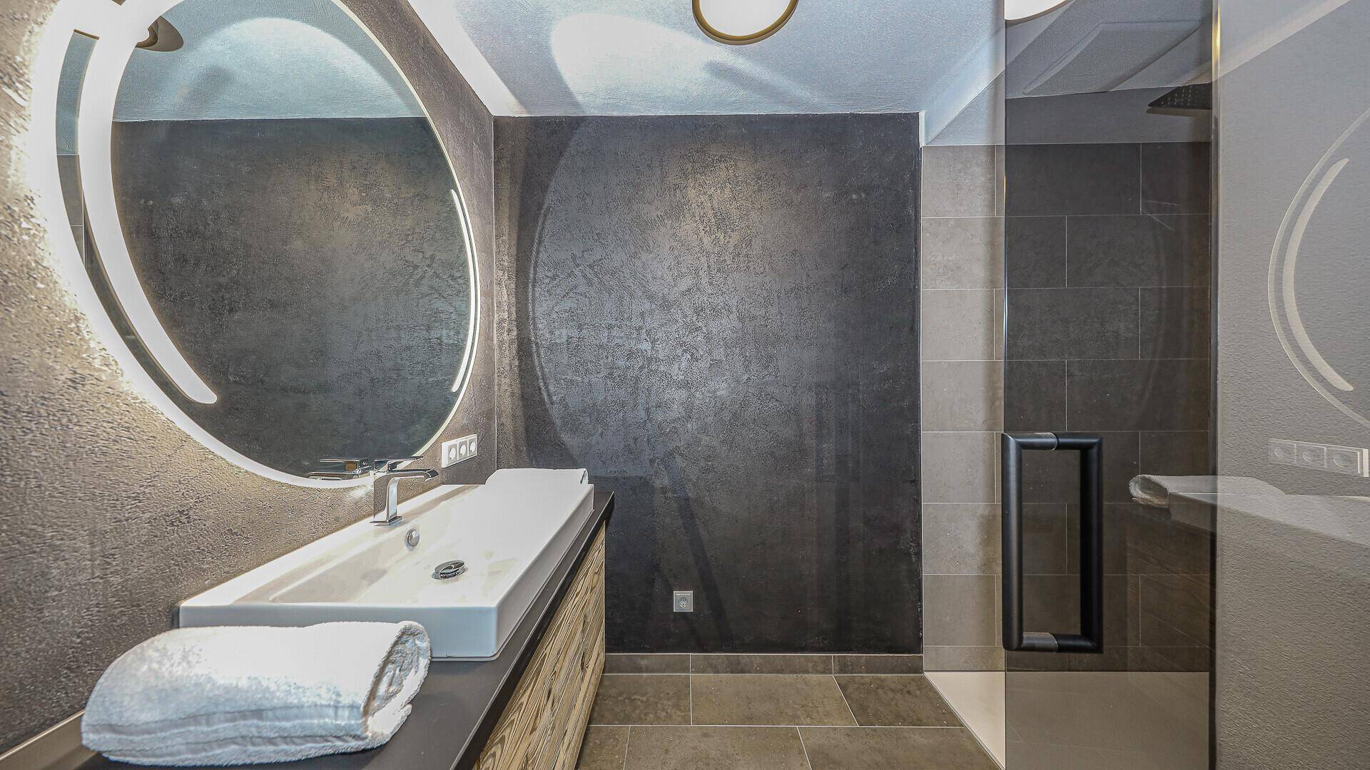 Elegantes Badezimmer mit großem beleuchtetem Spiegel, modernem Waschtisch und Dusche.