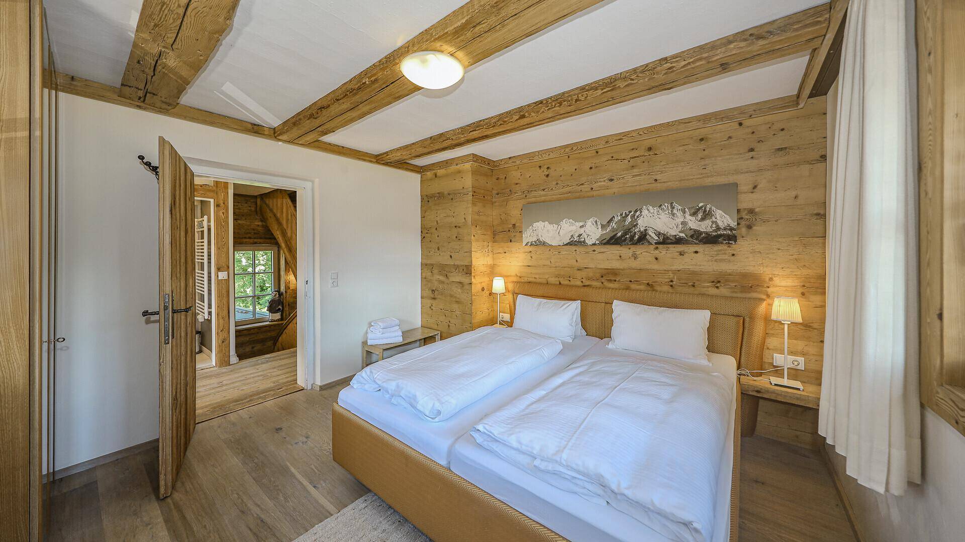 Helles Schlafzimmer mit Doppelbett, Holzbalken und alpiner Wanddekoration.