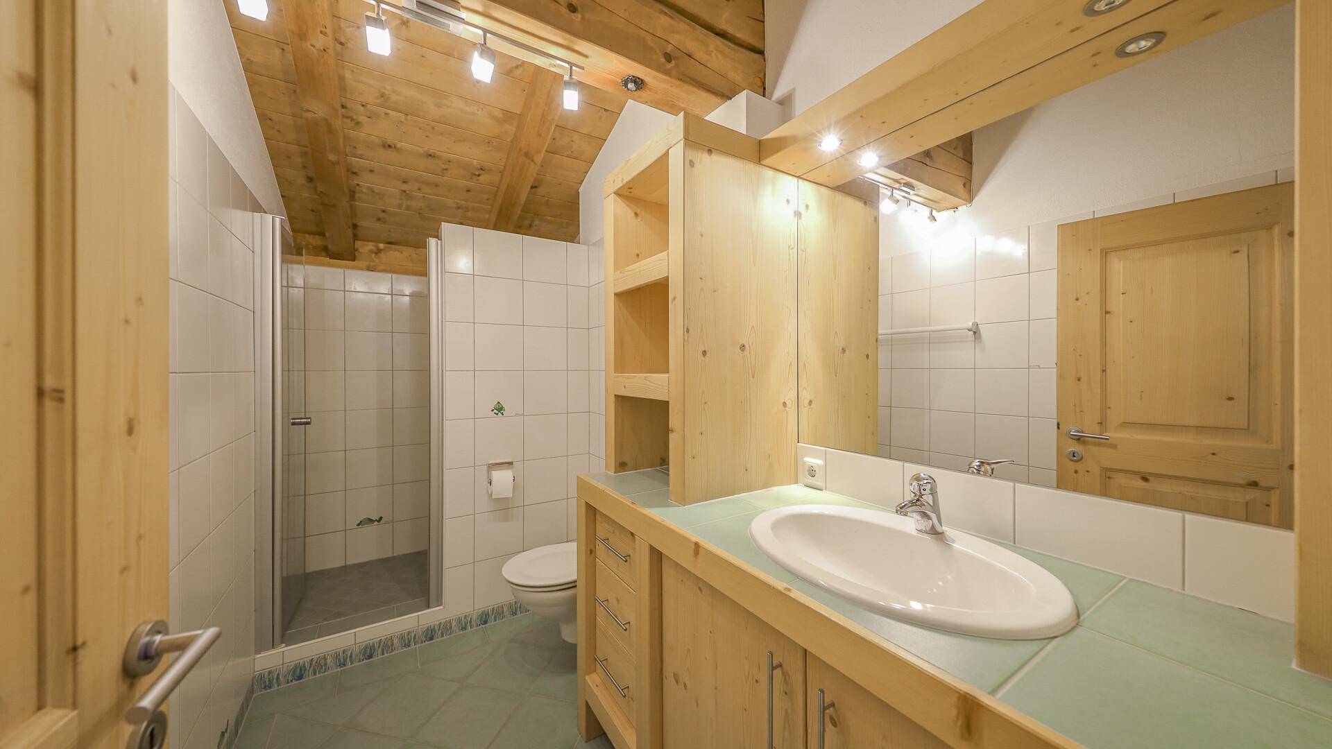 Badezimmer mit Dusche, Einzelwaschbecken, Holzschränken und Holzbalkendecke.