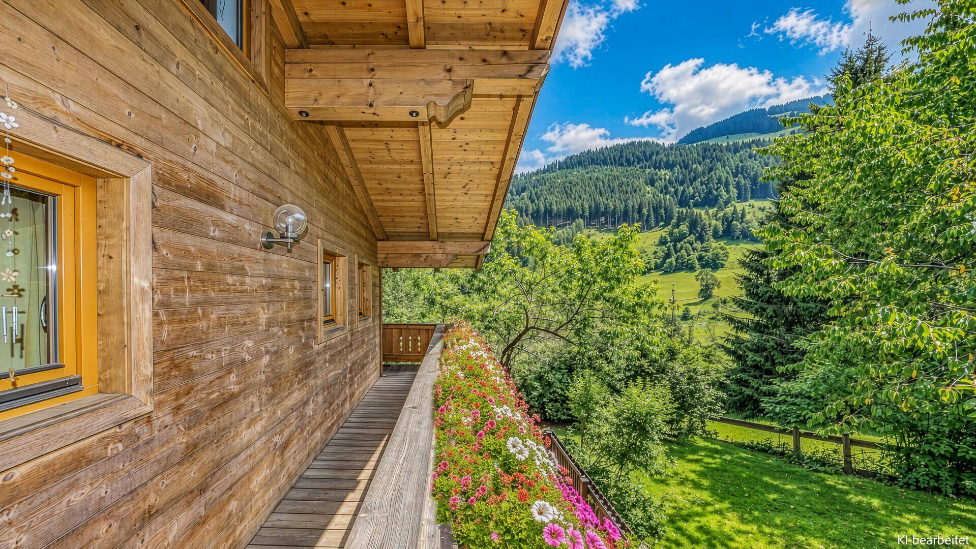 Geräumiger Holzbalkon mit Blumen und Blick auf die umliegenden Wälder und Berge.