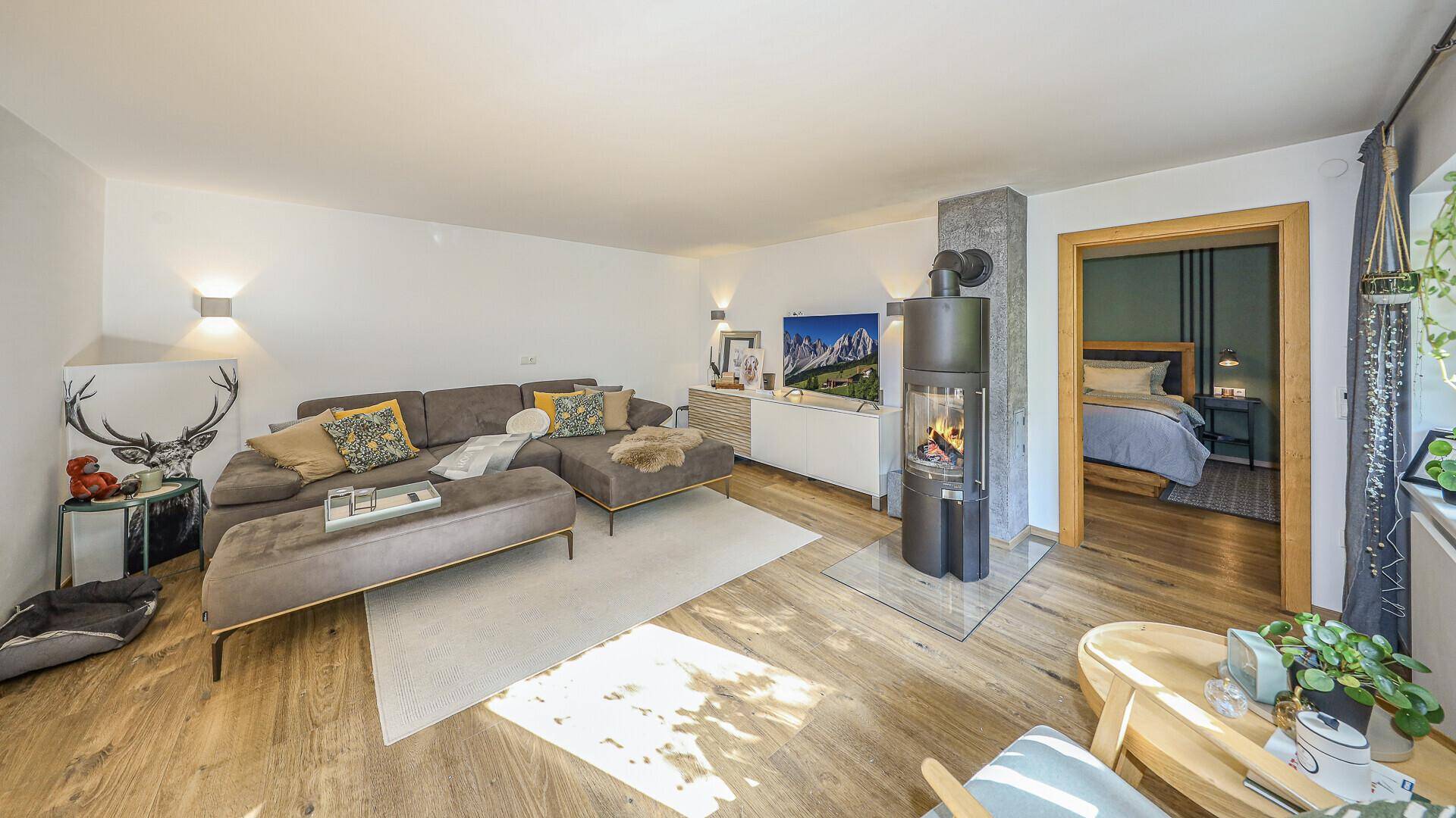 Helles Wohnzimmer mit Kaminofen und großem Sofa, mit direktem Zugang zu einem angrenzenden Schlafzimmer.