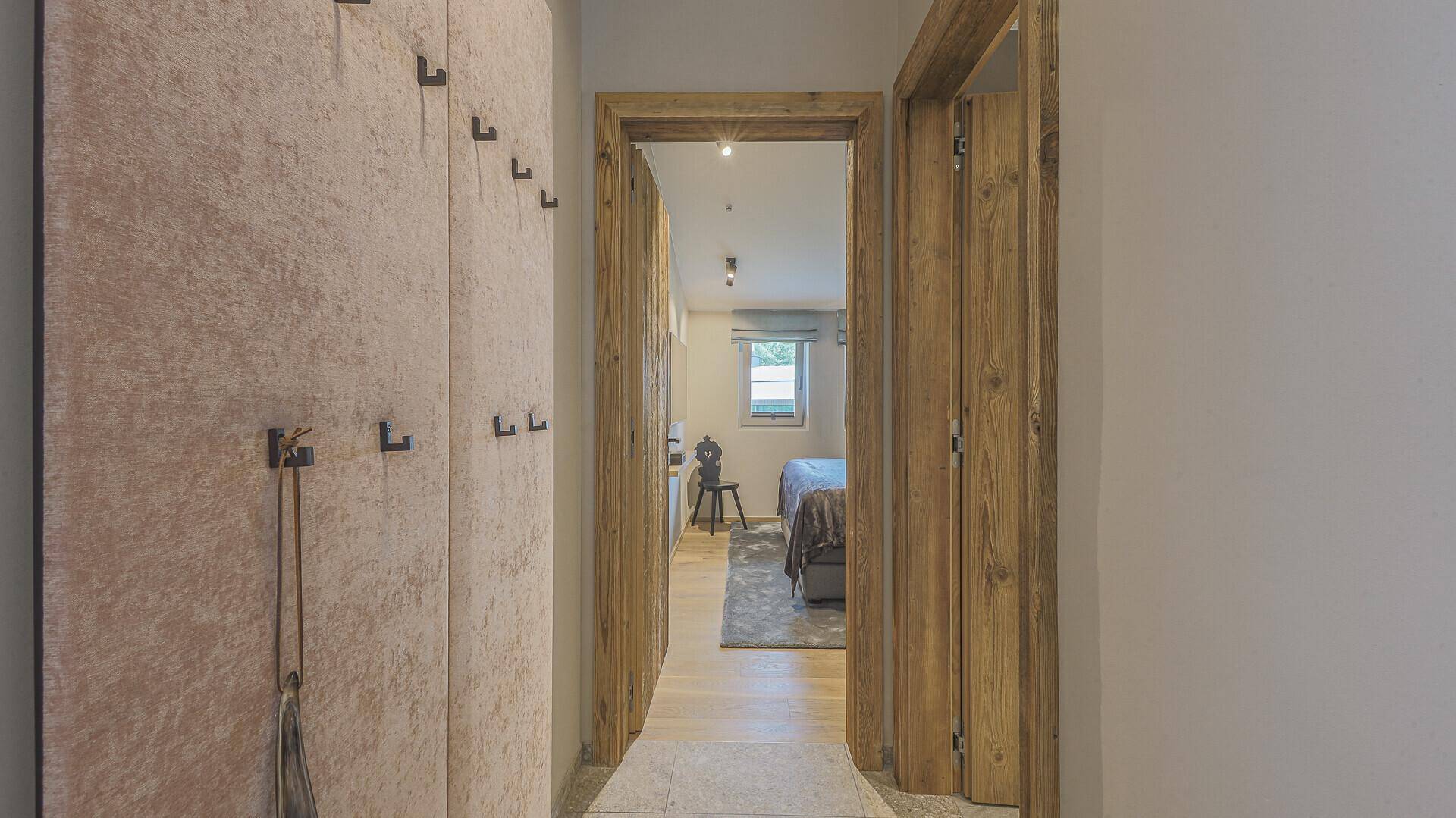 Flur mit Holztüren und Garderobe, der den Blick in ein Schlafzimmer freigibt.