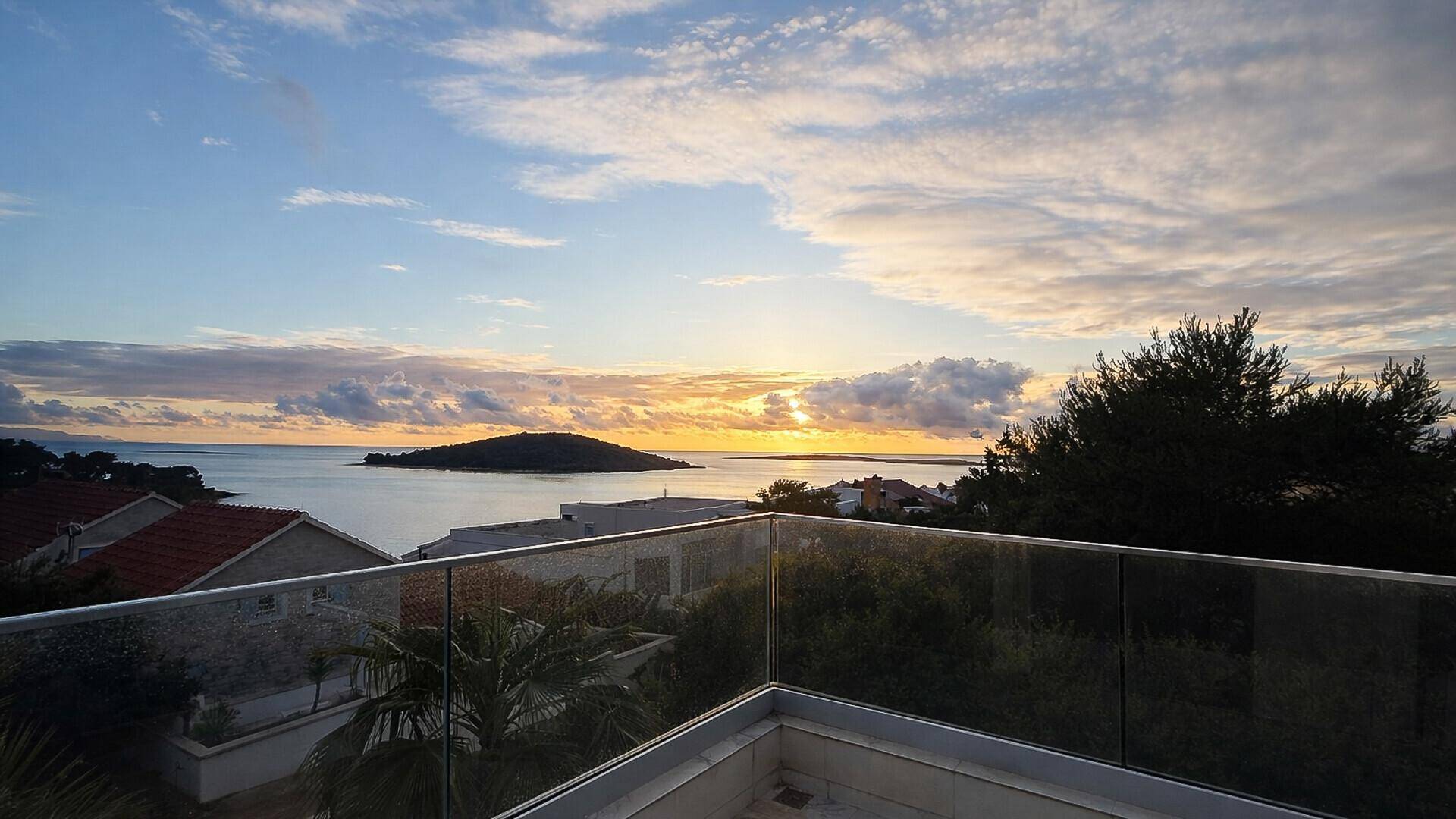 Atemberaubender Meerblick von einem Balkon mit Glasgeländer bei Sonnenuntergang.