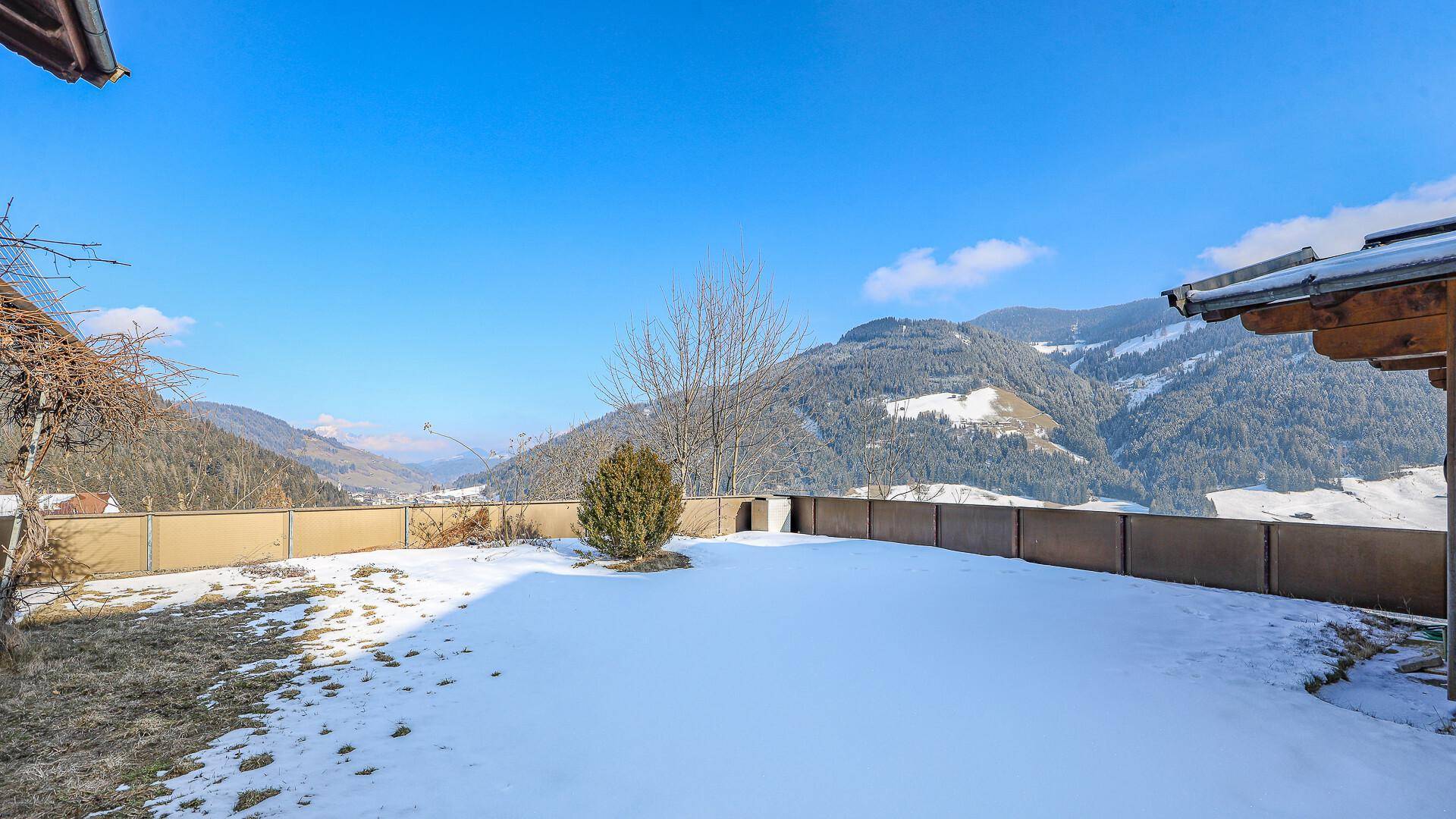 Verschneiter Gartenbereich mit Blick auf die umliegenden Berge an einem sonnigen Wintertag.