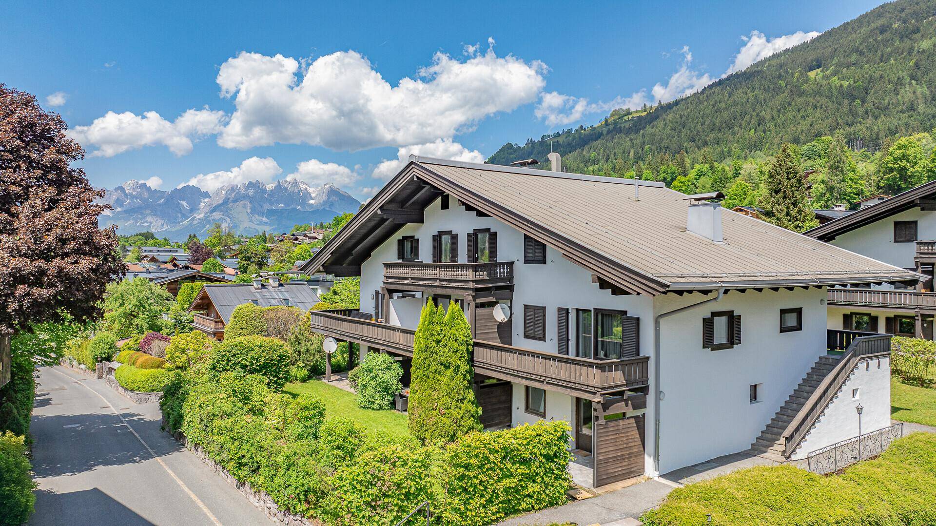 Attraktives Wohnhaus mit traditioneller Architektur, Balkonen und gepflegtem Gartenbereich vor Bergkulisse.