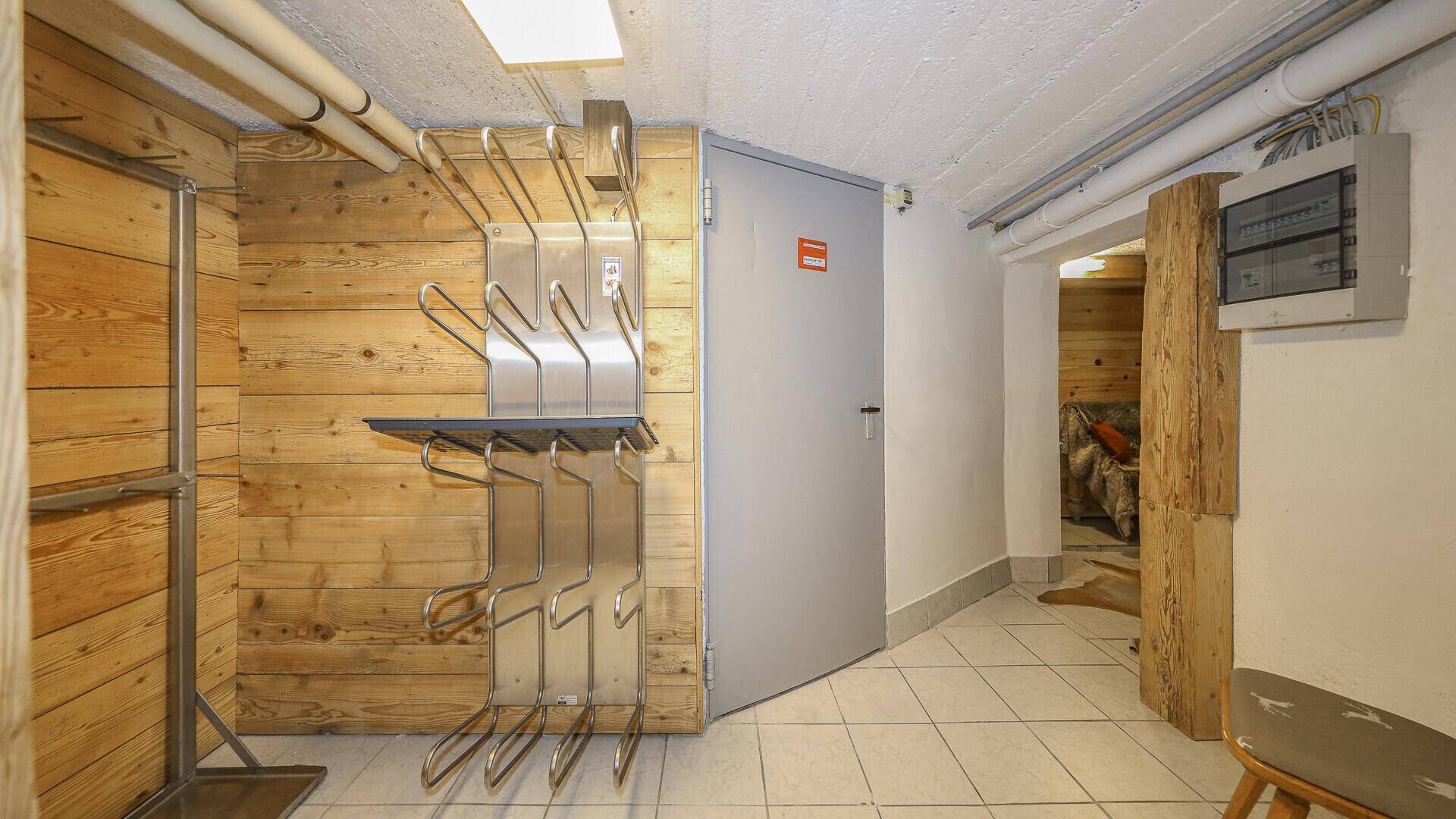 Praktischer Abstellraum mit Skischuh- und Skihalterungen, Holzvertäfelung und Fliesenboden.