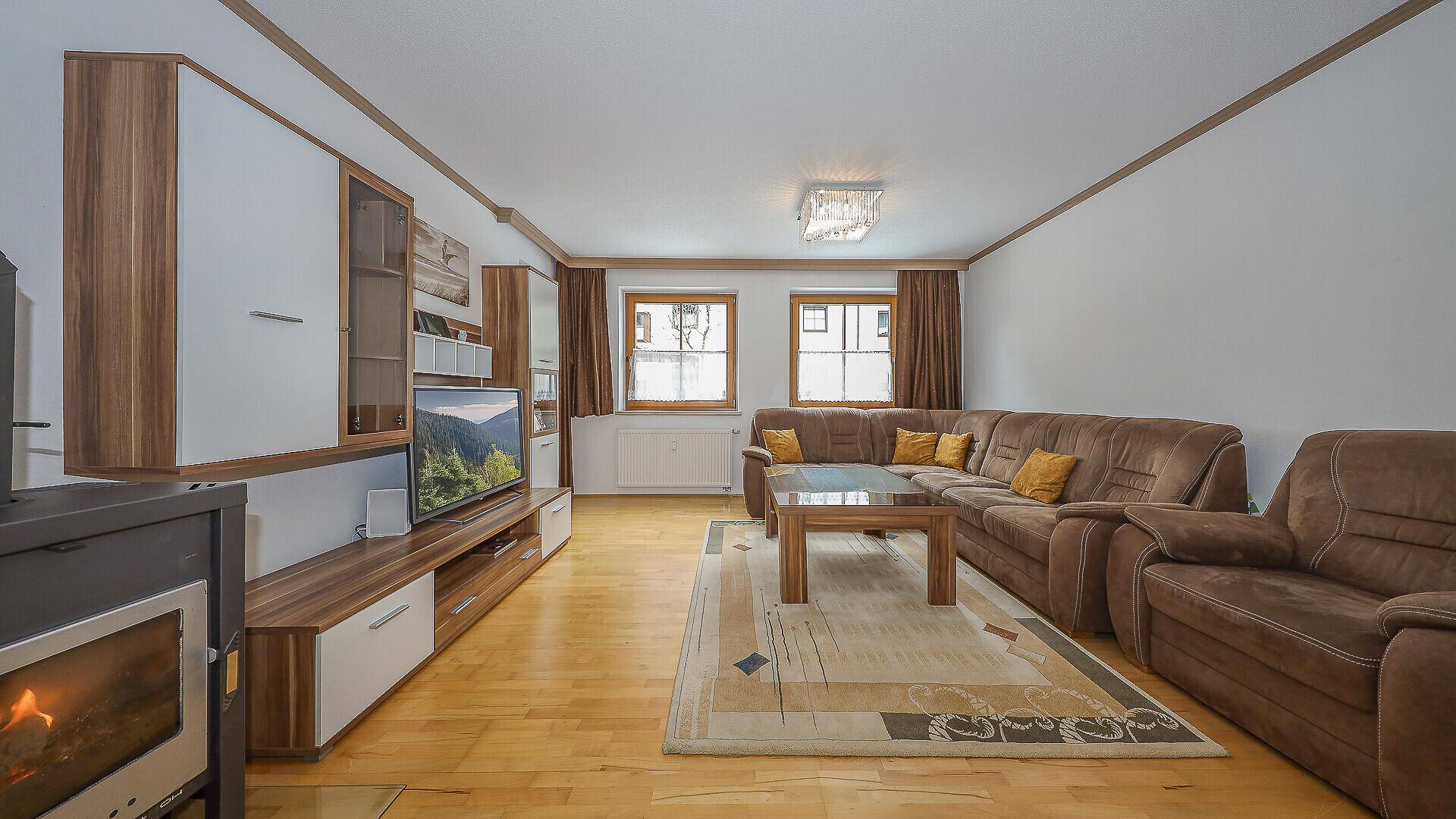 Geräumiges Wohnzimmer mit Kaminofen, großem Ecksofa und Holzmöbeln.
