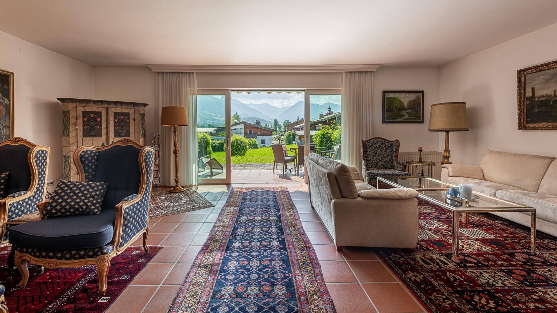 Helles Wohnzimmer mit Zugang zum Garten, traditionellen Möbeln und Panoramablick auf die grüne Bergwelt.